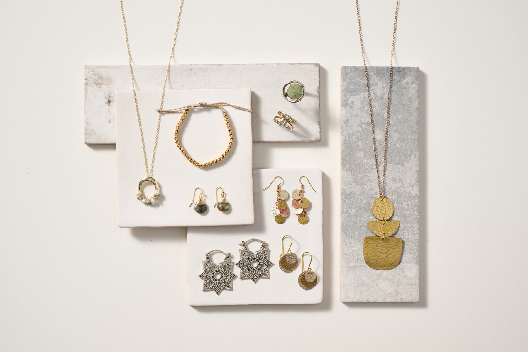 Display of jewelry including necklaces, earrings, and rings on white and gray background panels.