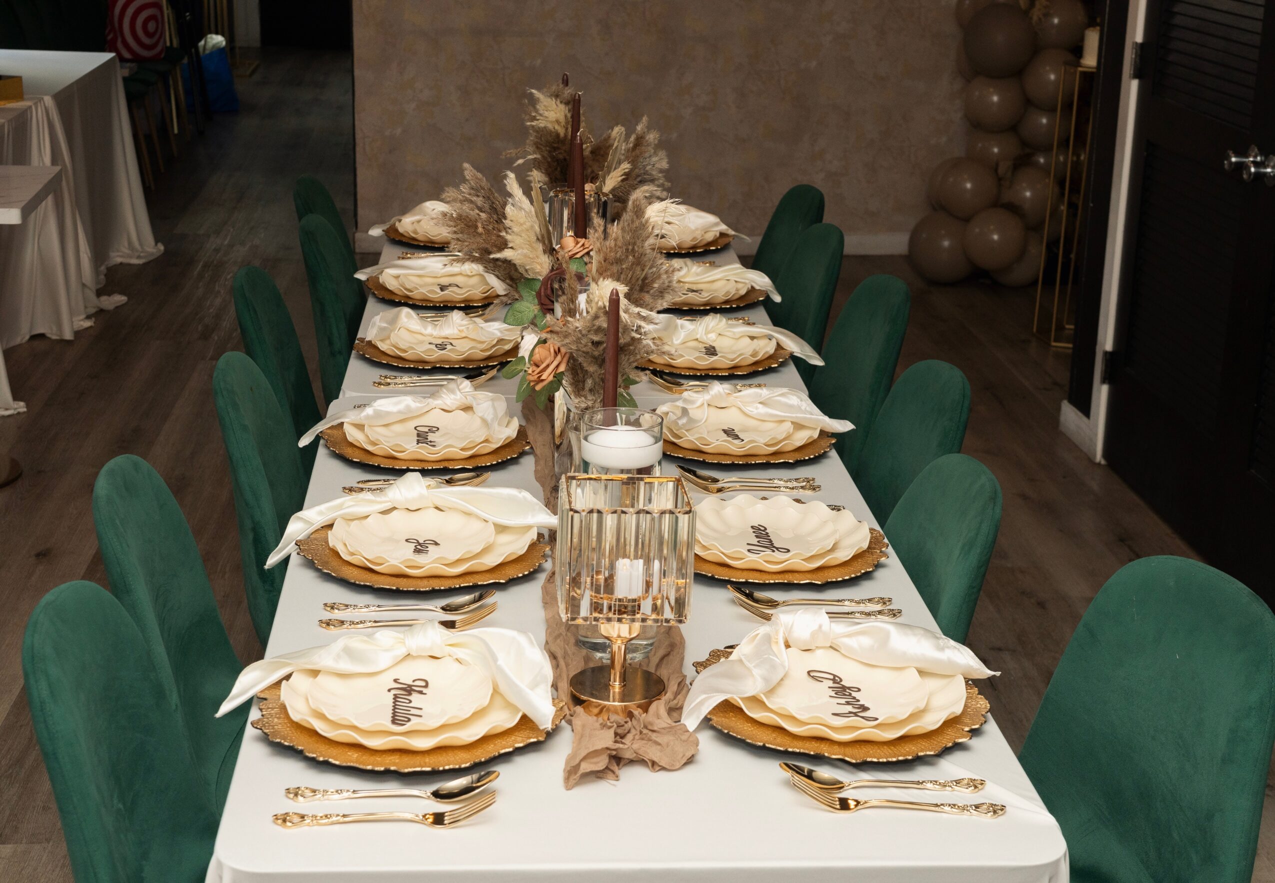 Long dining table set with plates, napkins, and cutlery, decorated with a floral centerpiece, surrounded by green chairs.