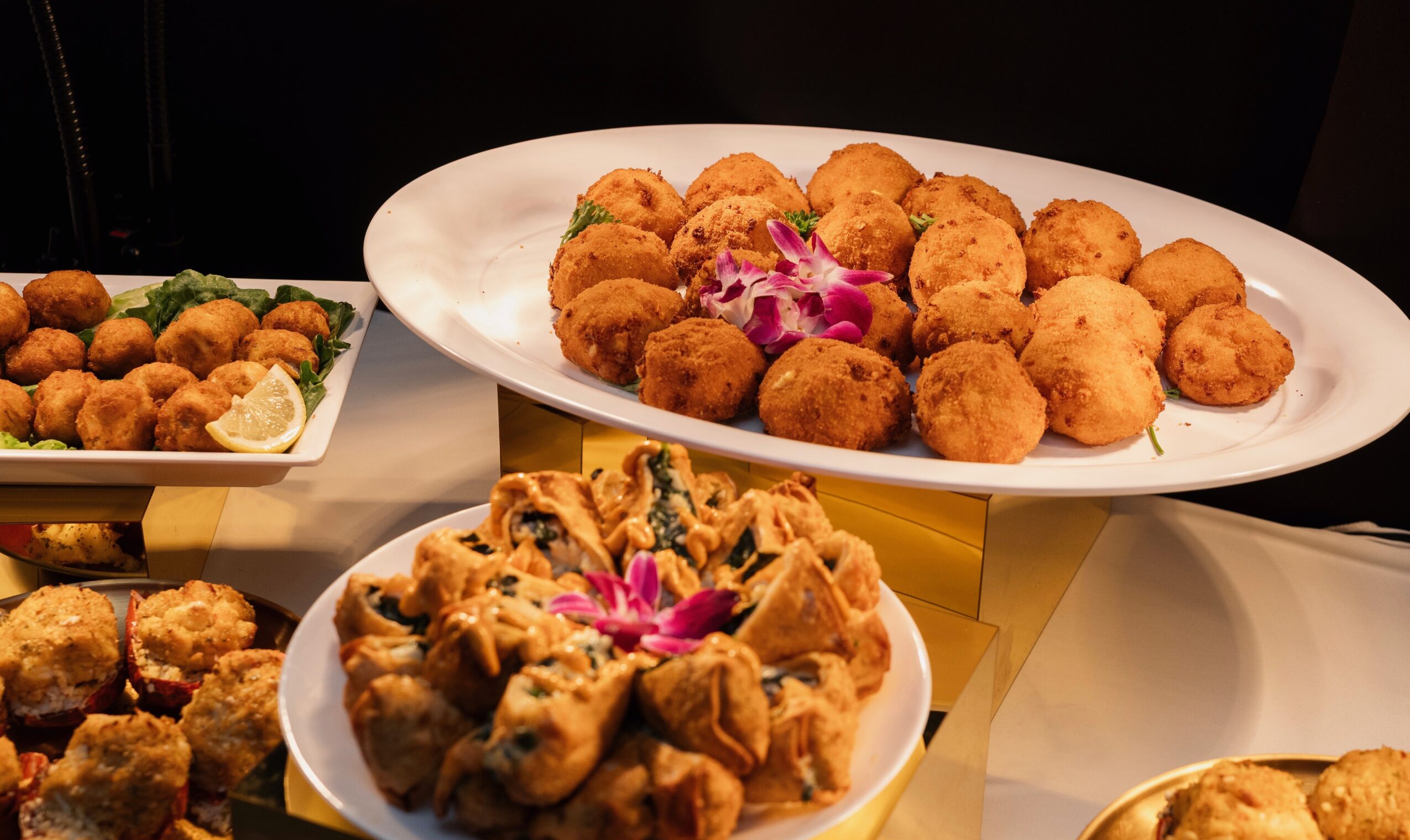Three dishes with fried food items on white plates, garnished with pink flowers and vegetables, on a table.