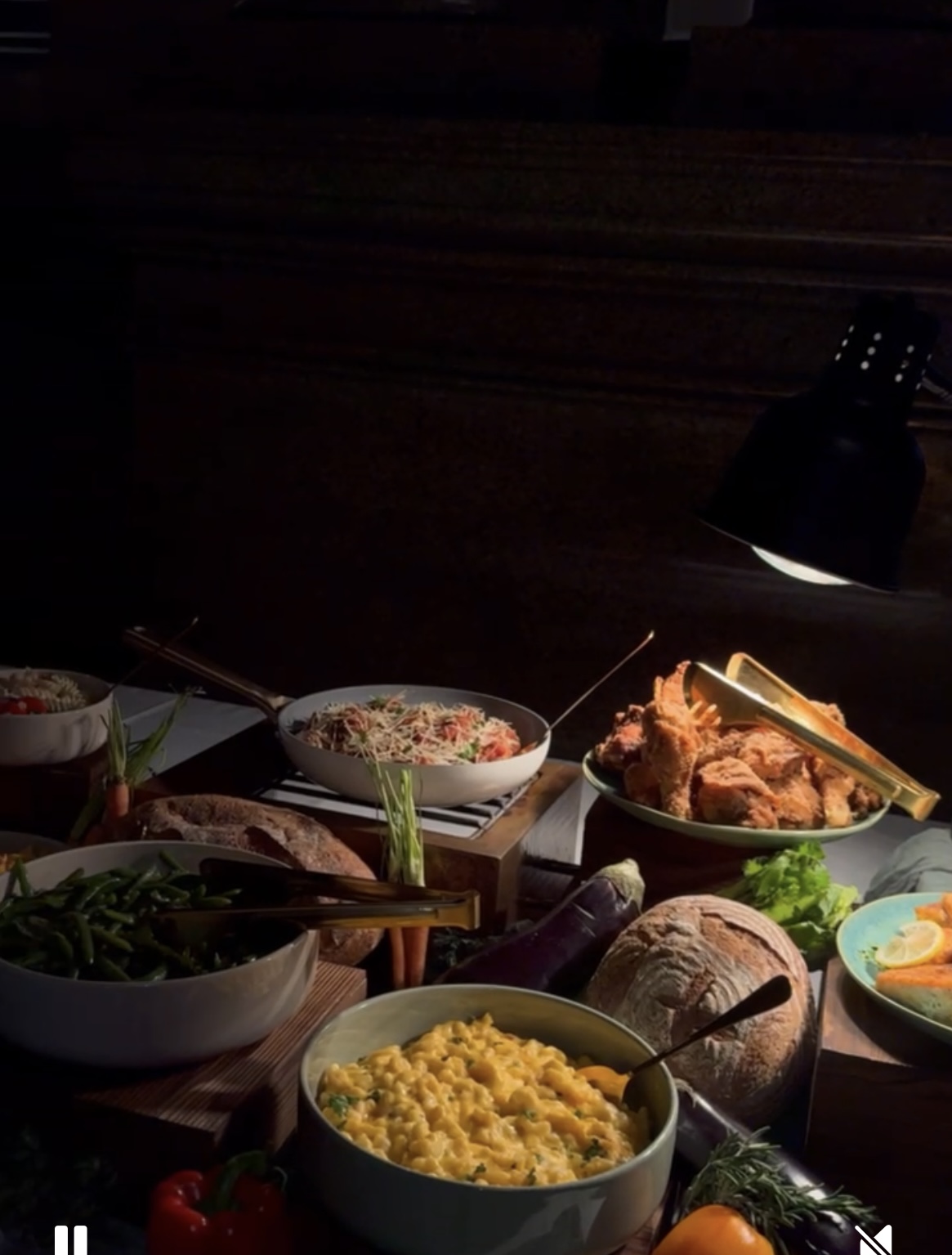 Assorted dishes on a table with a dark background, including rice, fried chicken, vegetables, and a lamp, illuminated by a light.
