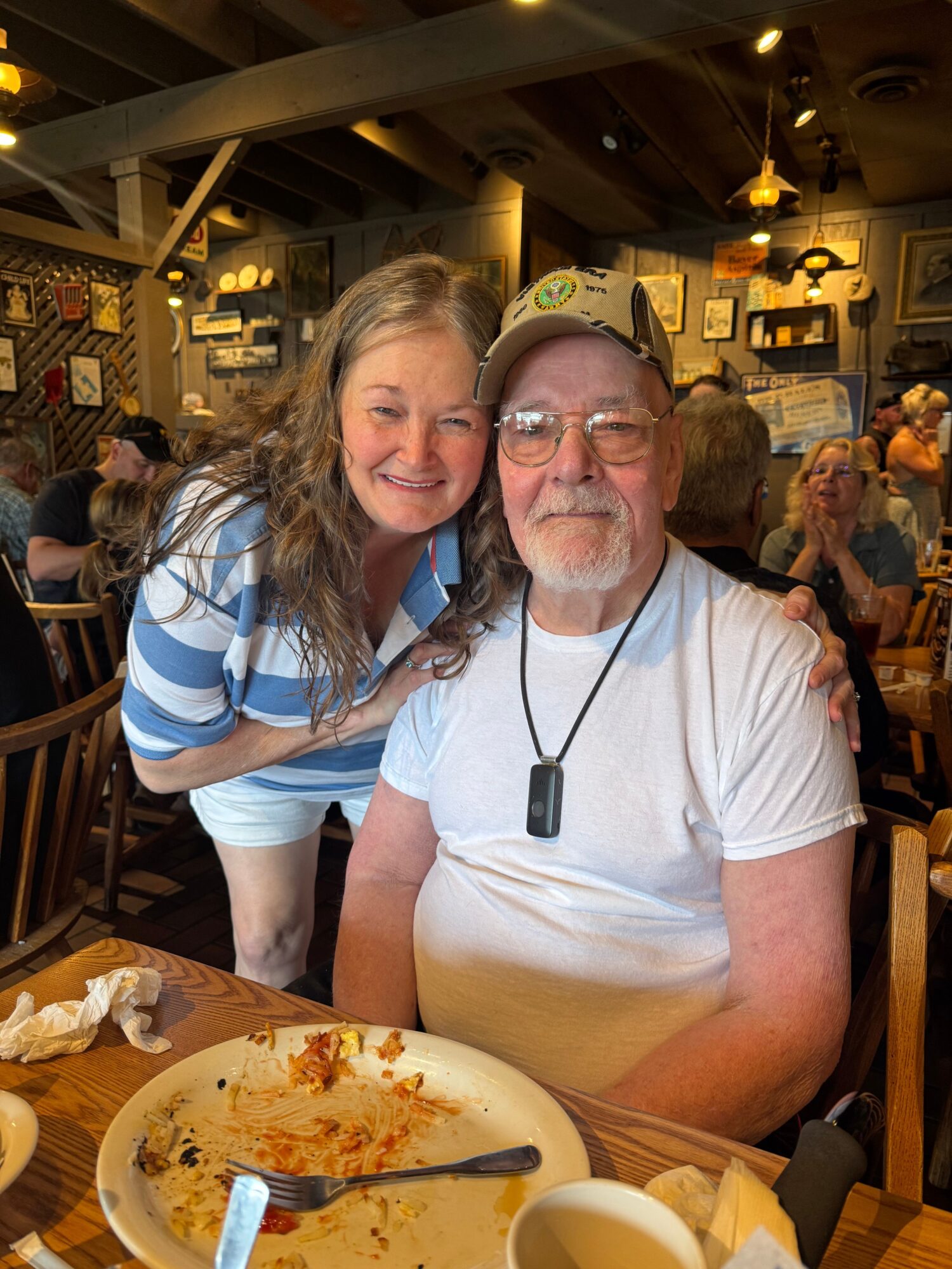 A woman with long hair and a man with glasses and a beard sit at a restaurant table, smiling, with a plate of food in front.
