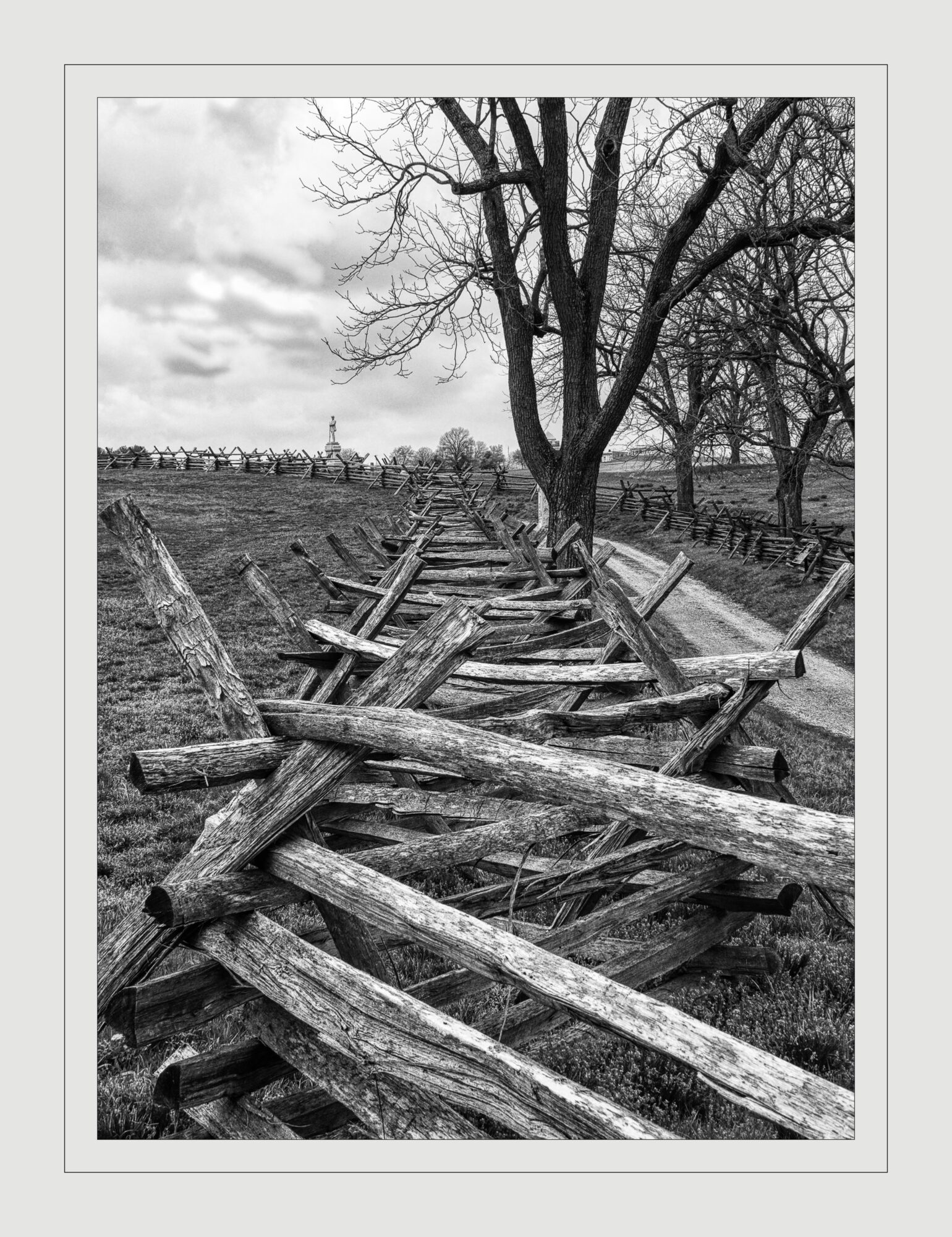 Wooden fence fallen and broken along a rural landscape with leafless trees and cloudy sky.