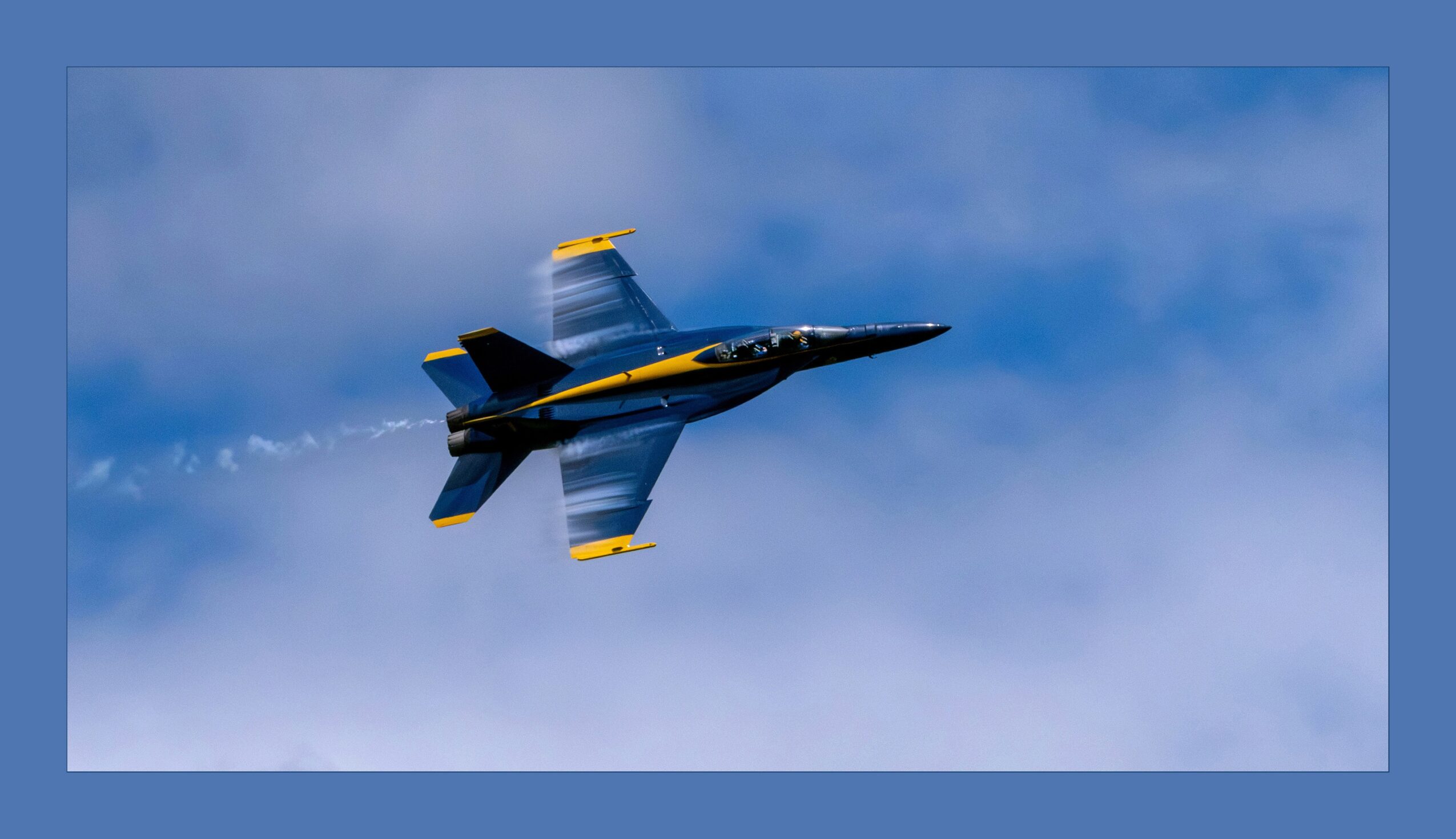 Fighter jet flying through blue sky with clouds, angled upward, with yellow and black markings, seen from below.