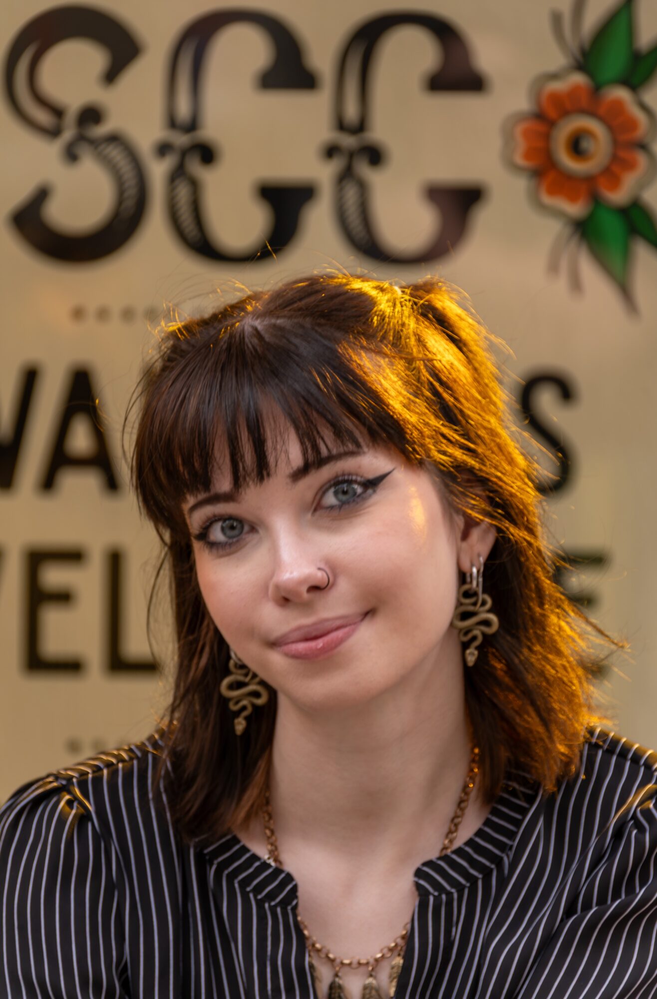 Young woman with dark hair and bangs, wearing earrings and a striped shirt, smiling at the camera.