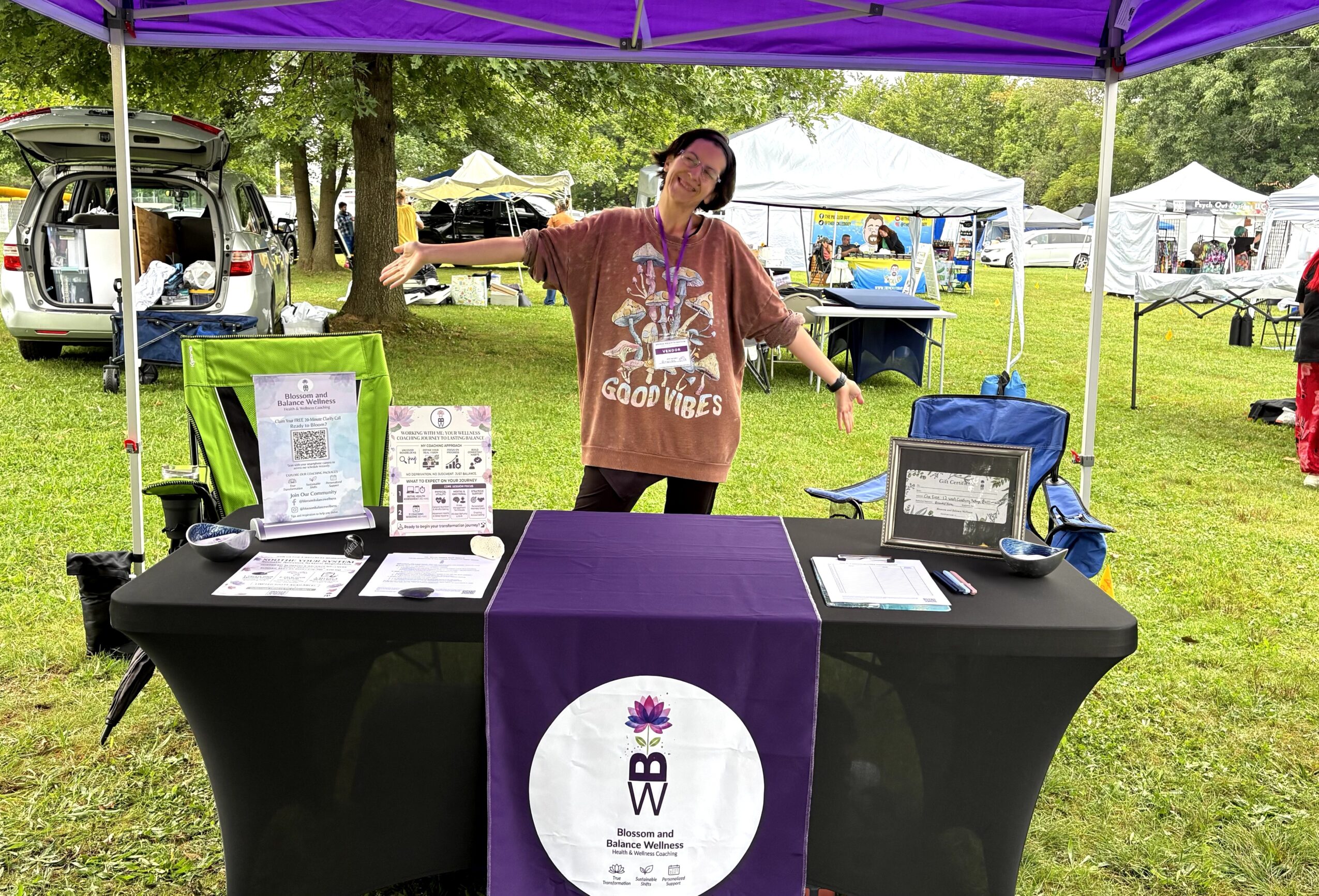 Person standing behind a table with informational materials under a purple canopy at an outdoor event.