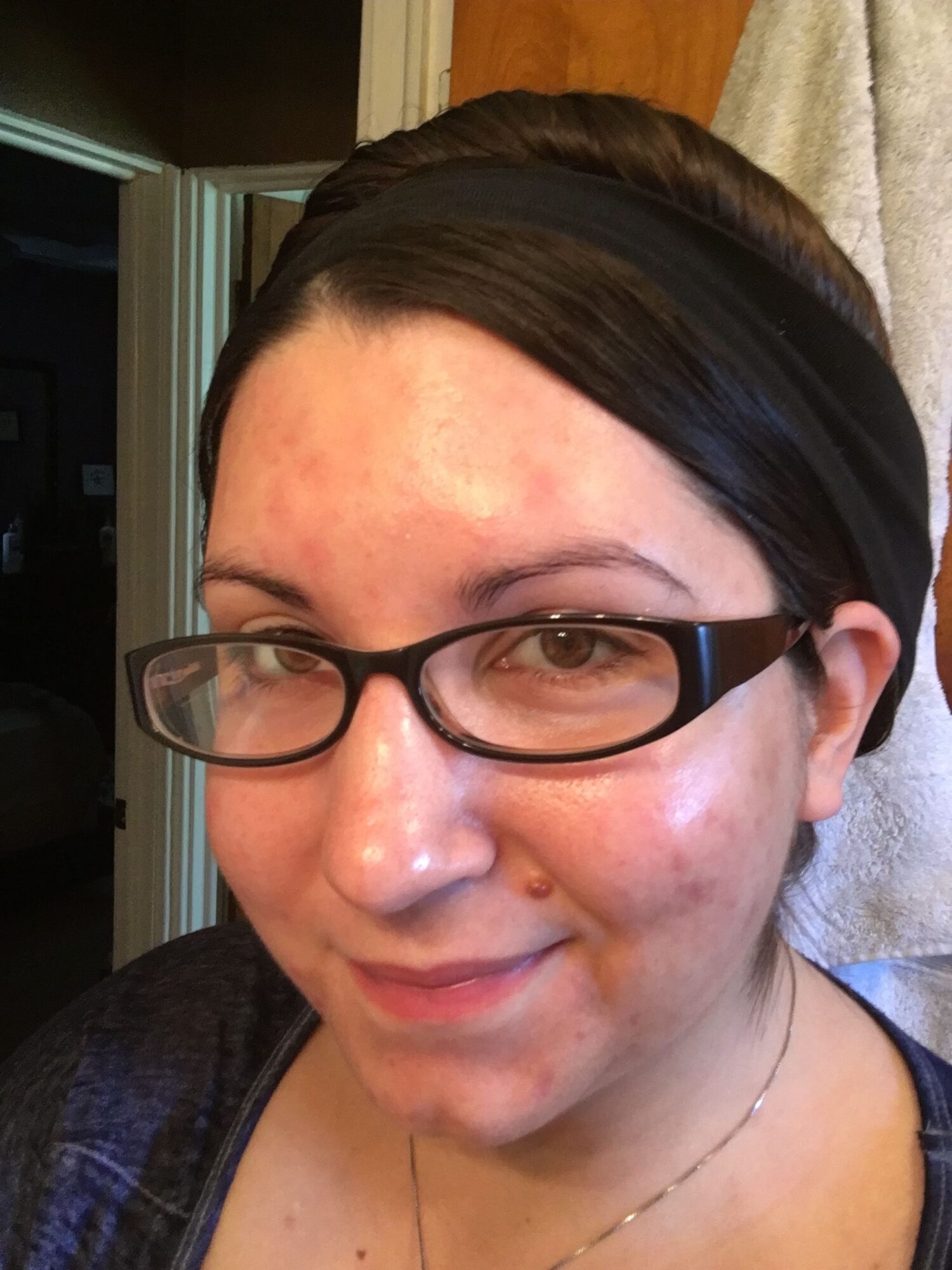 Close-up of a person with glasses, dark hair, and a headband, smiling slightly, indoors with a door in the background.