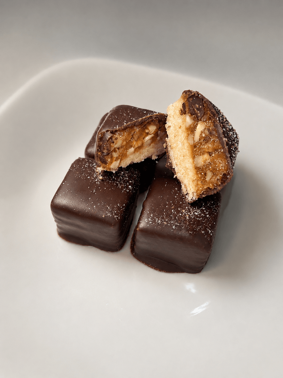 Three chocolate-covered rectangular confections with a caramel and biscuit filling, one cut in half, on a white plate.