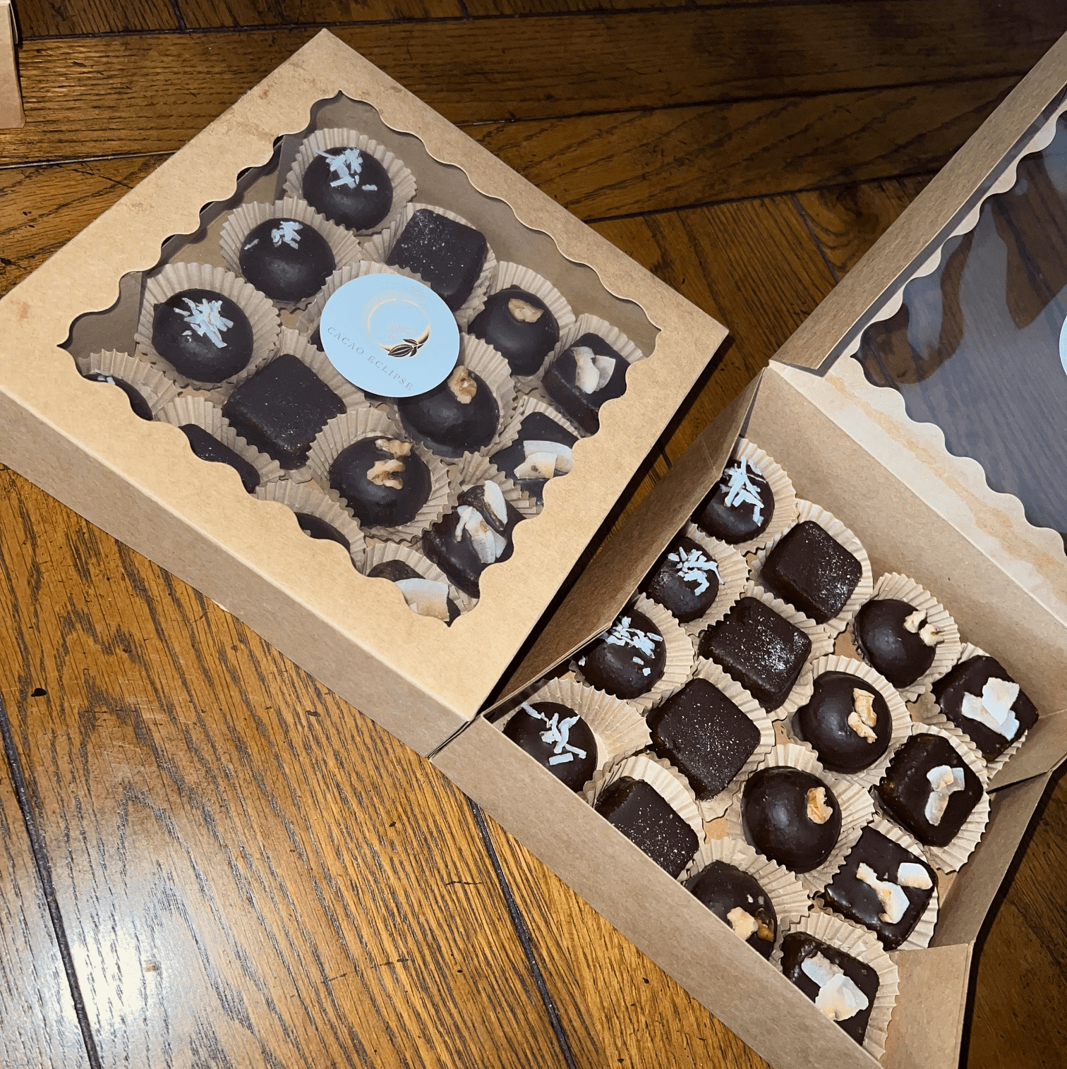 Two open boxes of assorted chocolates on a wooden surface, with various shapes and designs on the chocolates.