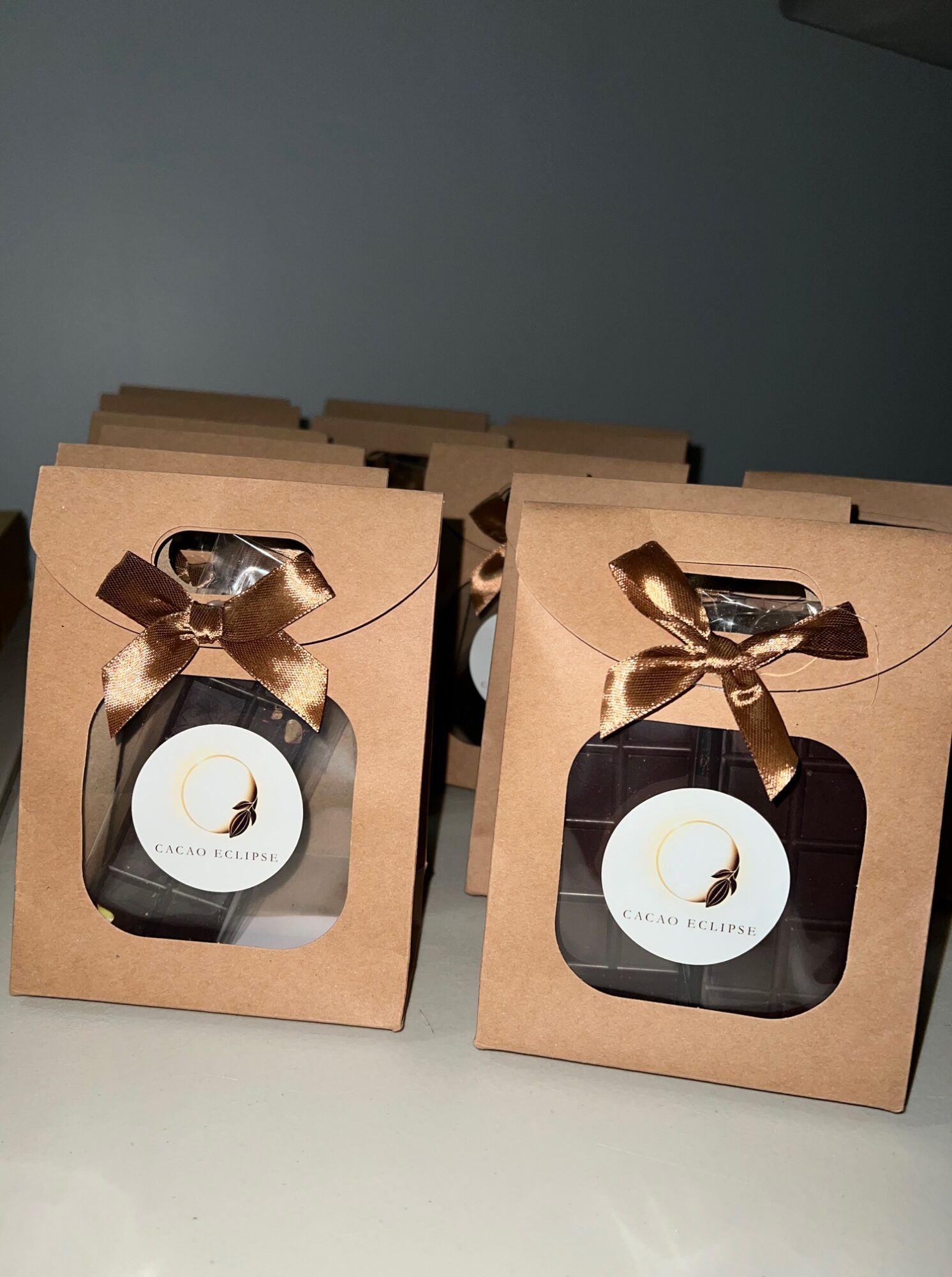 Two gift boxes with bottles inside, each with a round label and a gold ribbon bow, stacked on a white surface.