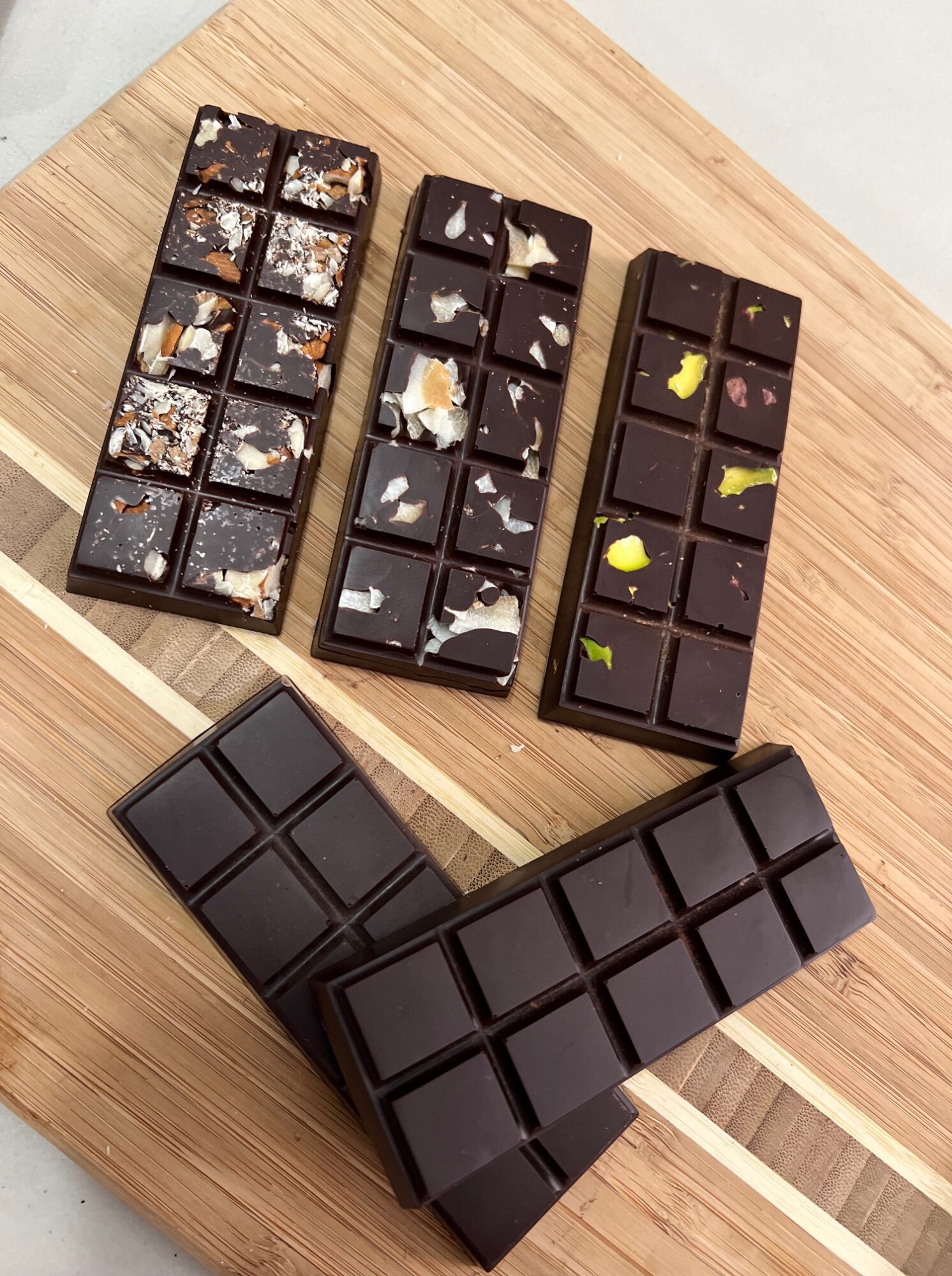 Four chocolate bars with different toppings on a wooden surface, some broken into pieces.