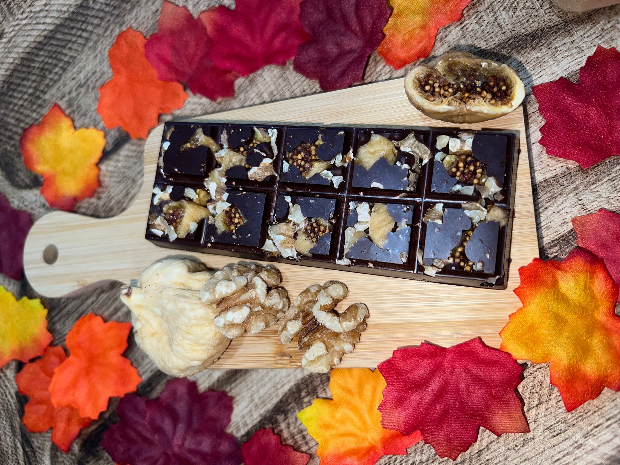 Chocolate bars on a wooden board surrounded by colorful autumn leaves and a halved passion fruit.