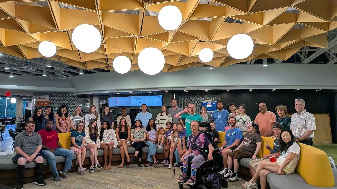 Group of people in a modern indoor space with yellow seating and decorative ceiling lights.