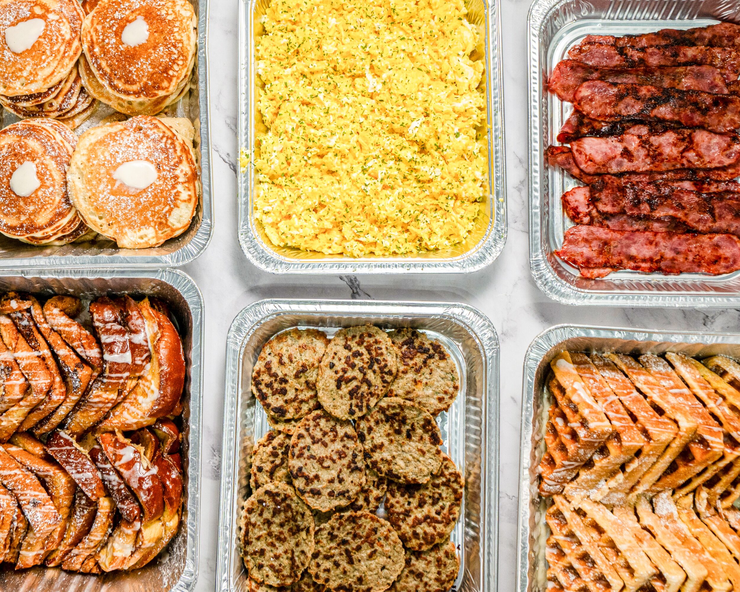 Six trays of food including muffins, yellow rice, beef jerky, sausage patties, cookies, and a pie.