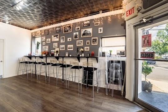 Interior of a cafe with a wall decorated with photos, a counter with bar stools, and a glass door with a closed sign.