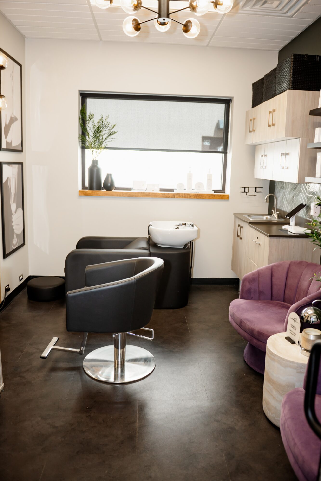 Salon with black and purple chairs, a window with plants, and a white cabinet, illuminated by a ceiling light.
