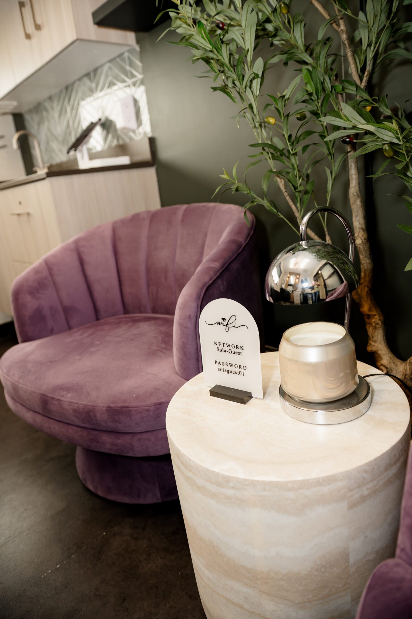 Purple velvet armchair next to a round white table with a plant, mirror, and decorative items, in a cozy interior setting.