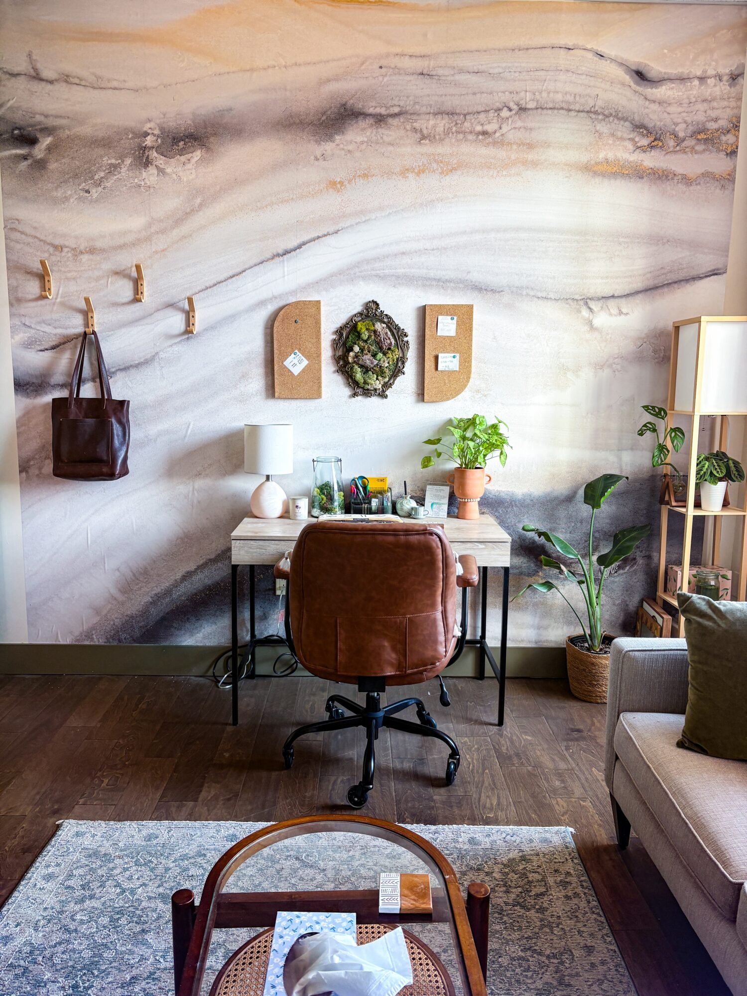 Home office with desk, brown chair, plants, wall decor, and a window with a lamp, in a cozy room.