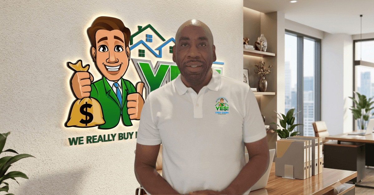 Man in white polo shirt standing indoors with a cartoon character and house logo on wall behind him.