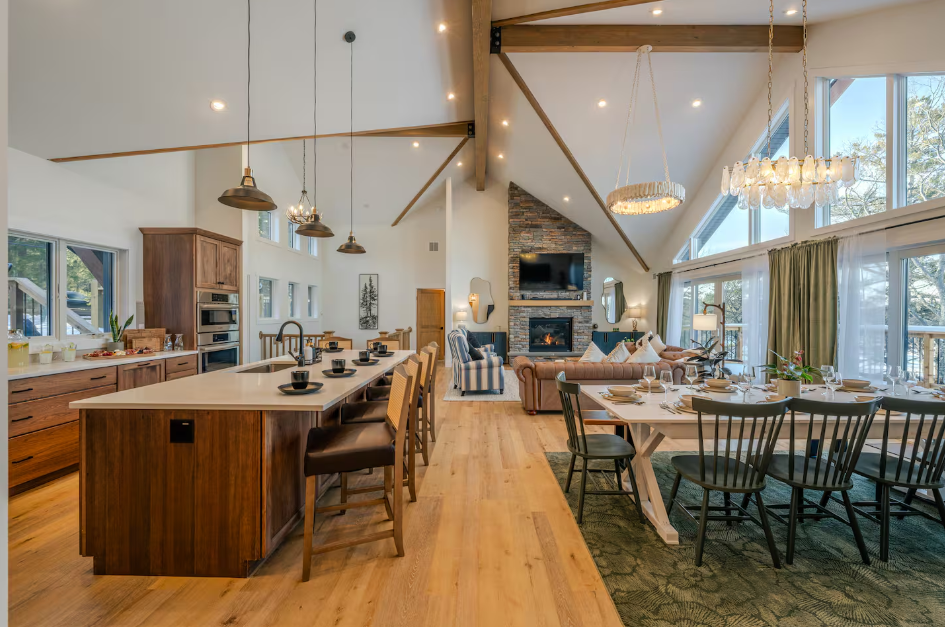 Open-concept kitchen and dining area with wooden floors, high vaulted ceiling, large windows, and modern decor.