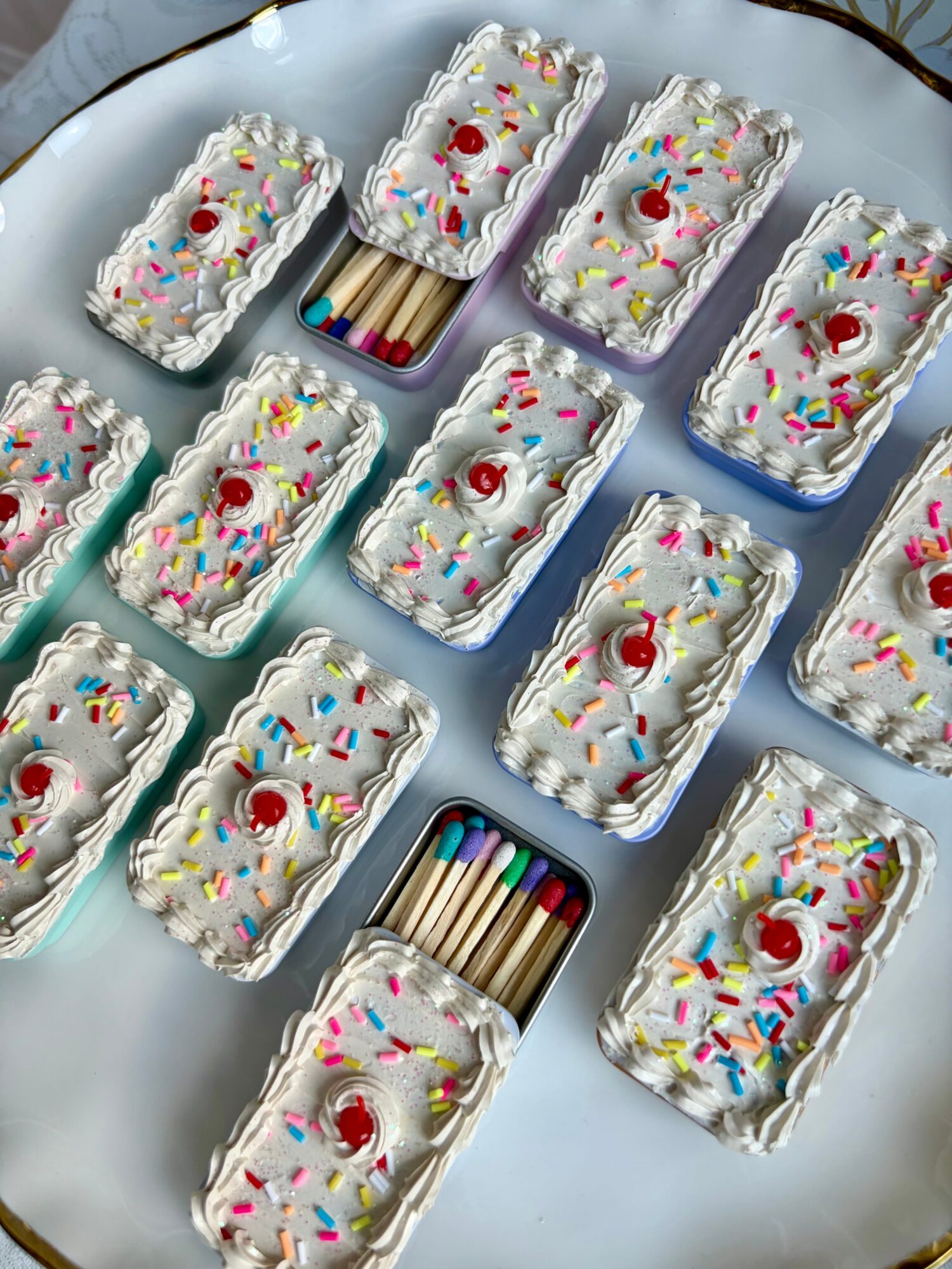 Rectangular cakes decorated with white icing, colorful sprinkles, and cherries, arranged on a silver tray with a box of colored pencils.