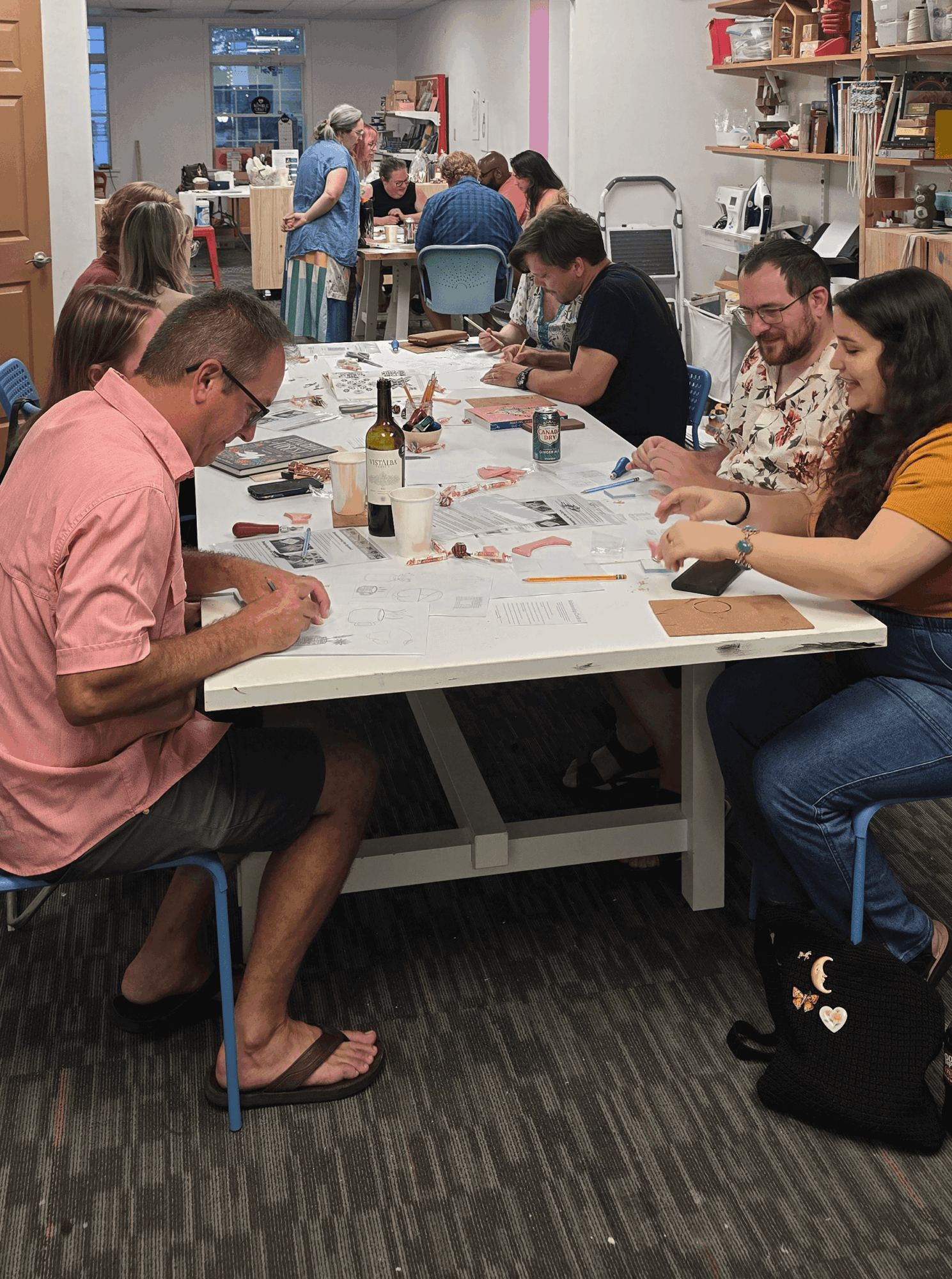 People sitting around a table playing a game, with bookshelves and a group in the background, in a room with pink and white walls.