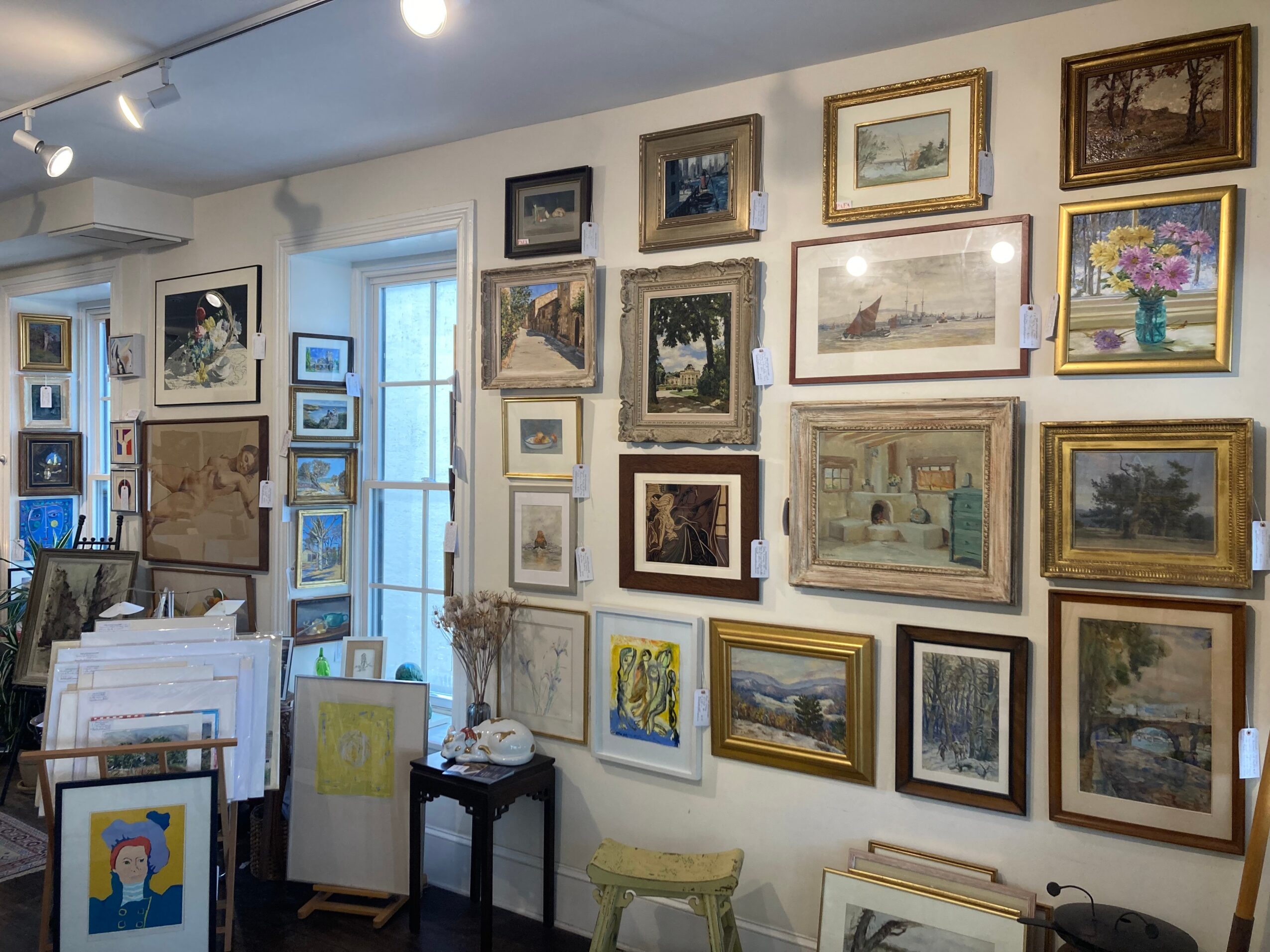 Gallery wall with framed paintings and photographs, a small table, and a window with natural light.
