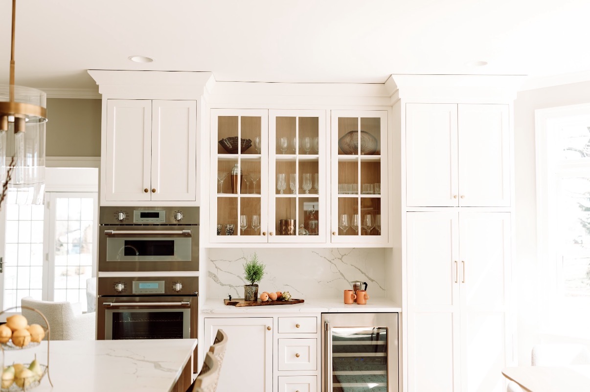 Kitchen with white cabinets, glass-front upper cabinets, built-in oven, and a wine cooler, bright and well-lit.