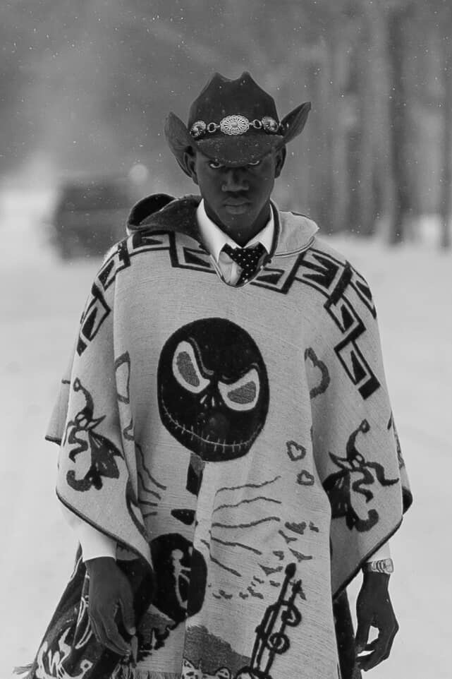 Person wearing a hat and patterned poncho with a skull design, standing outdoors in a snowy environment.