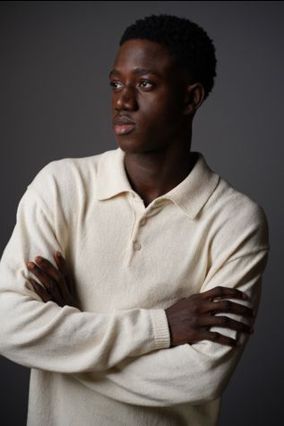 Person lying sideways with arms crossed, wearing a cream sweater, against a dark background.