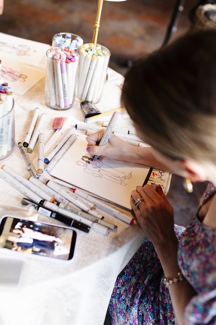 Person drawing on paper with colored markers, surrounded by art supplies and cotton candy on a table.