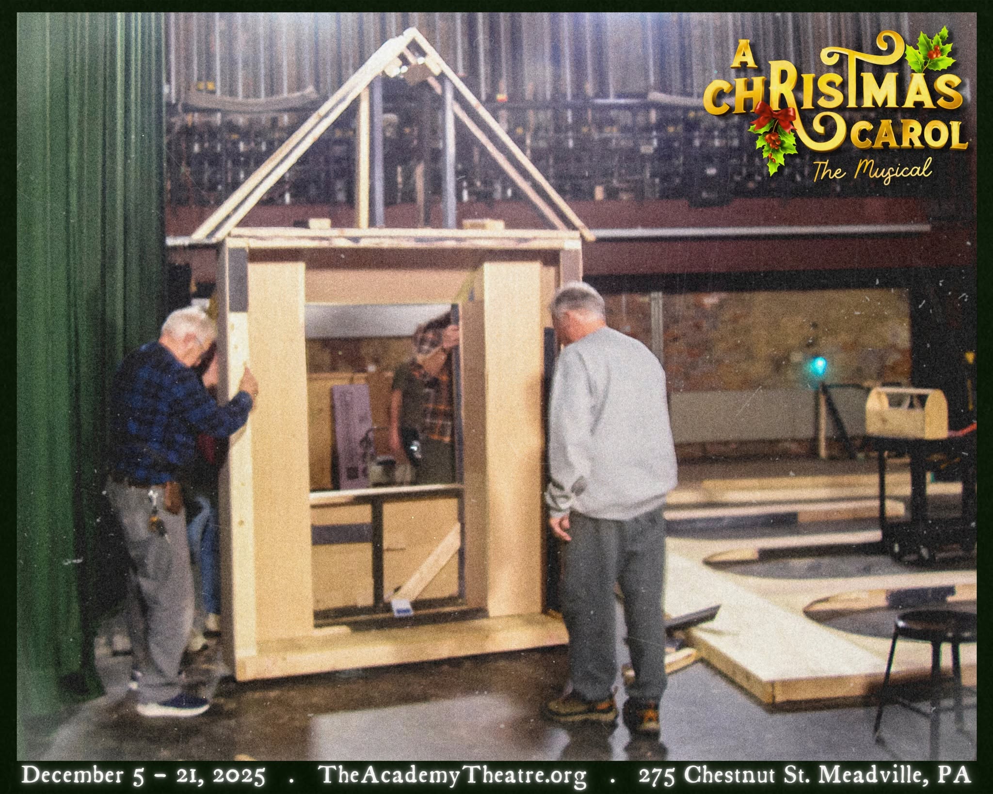 Three people work on a wooden set piece for a Christmas play, with a green curtain and stage equipment in background.