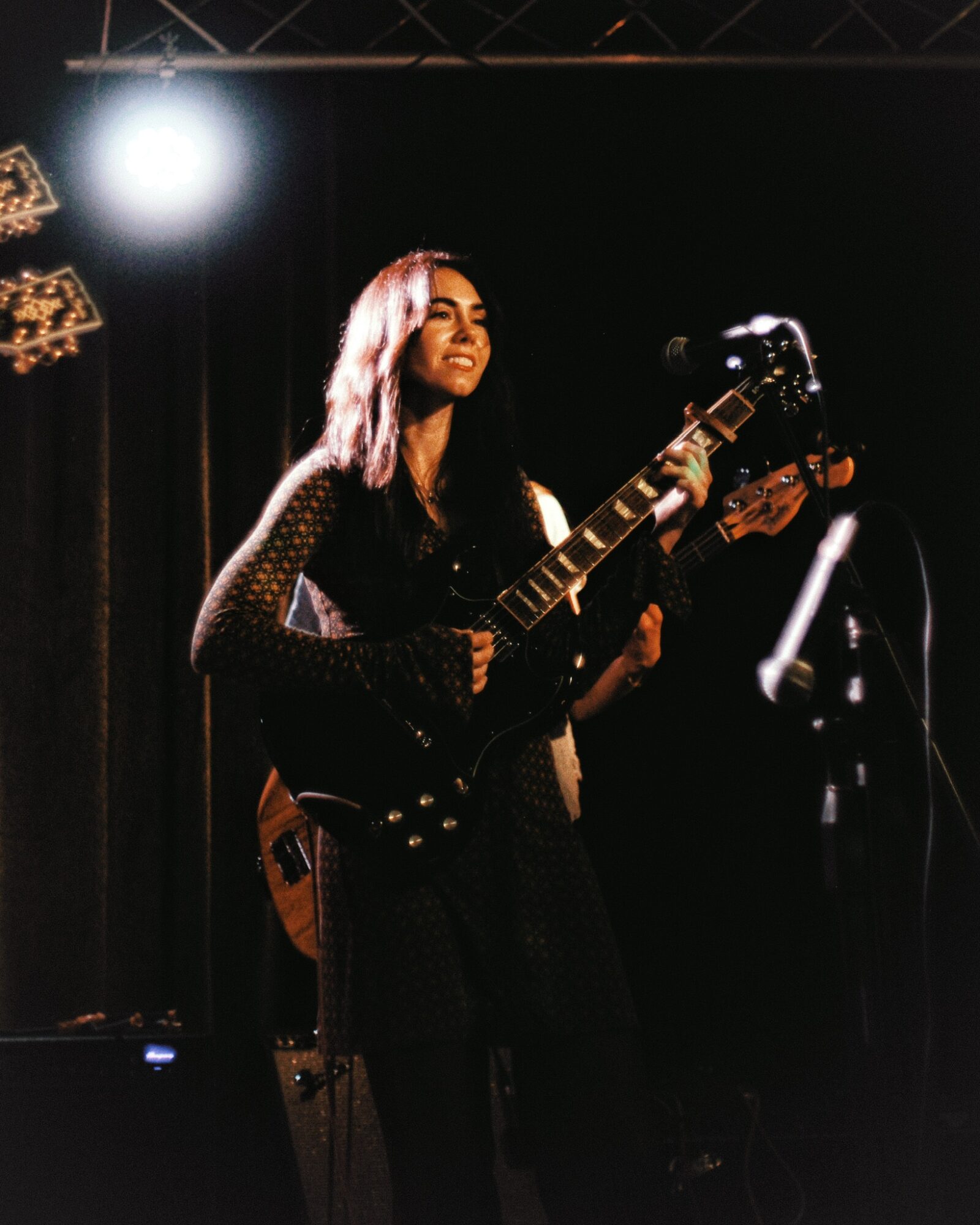 Woman playing an electric guitar on stage with a dark background and stage lighting.