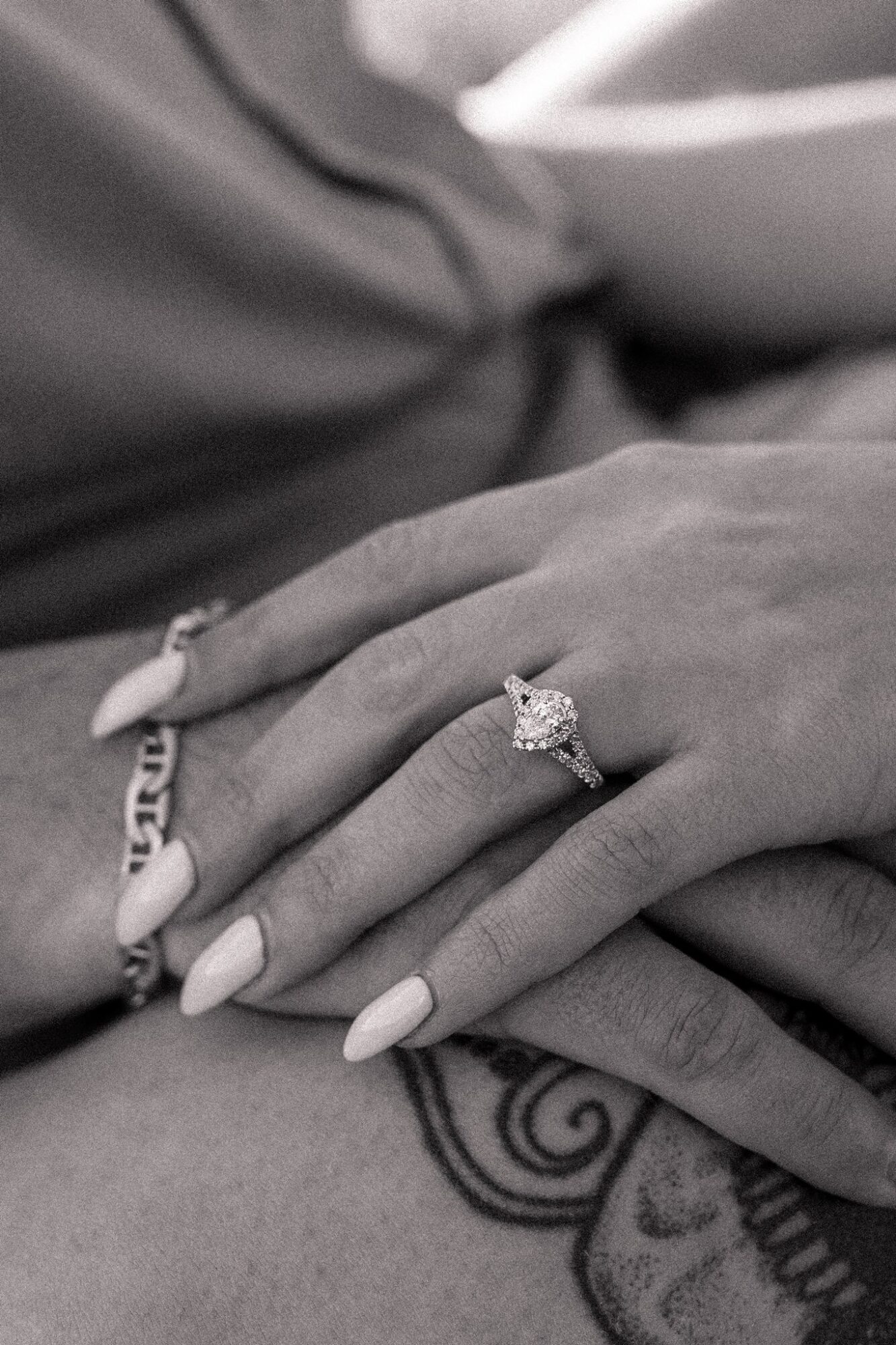 Close-up of a person's hand with an engagement ring, showing manicured nails and a tattoo on the wrist.