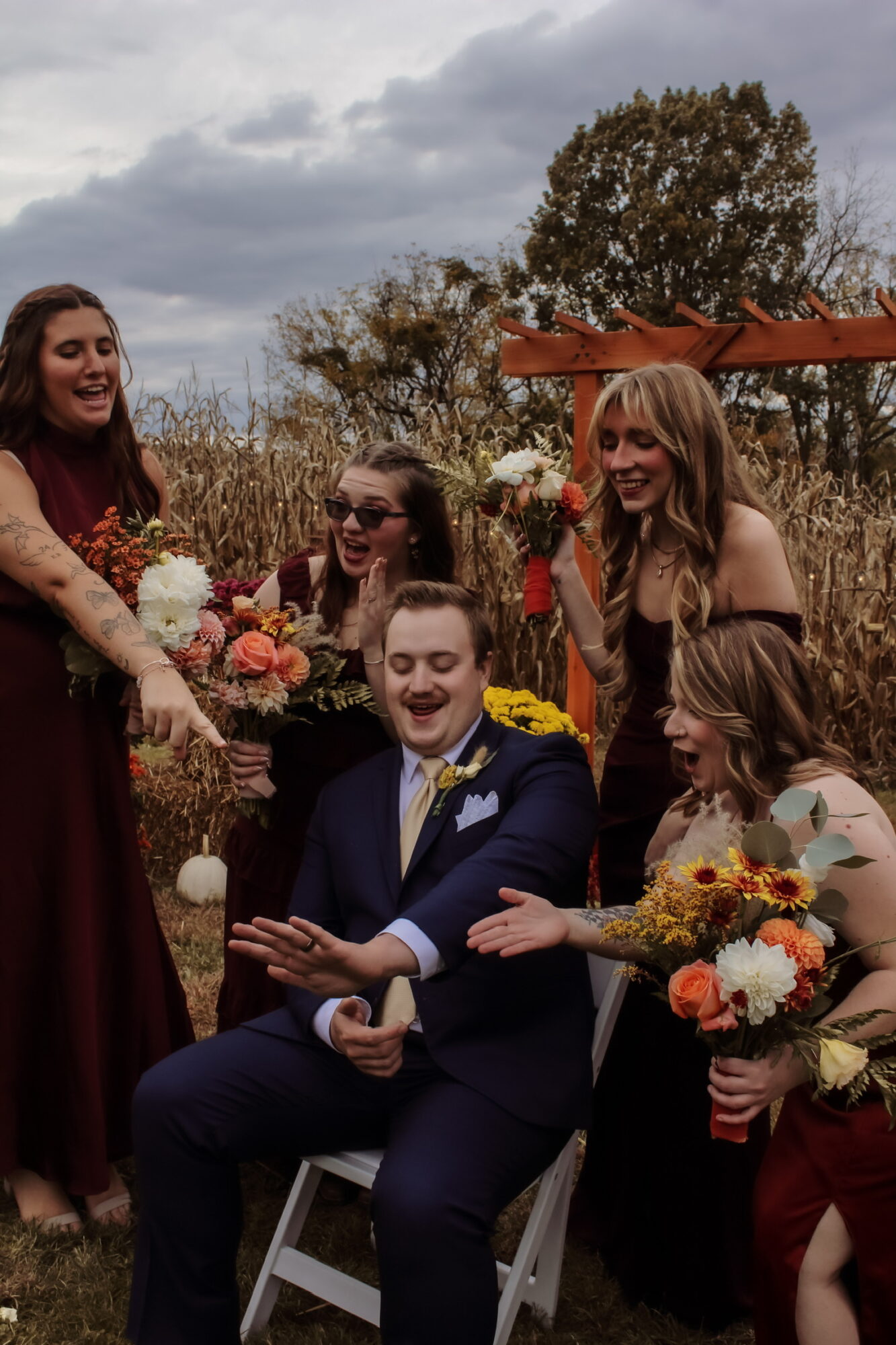 Group of five people outdoors, smiling, with flowers, under cloudy sky, trees in background.