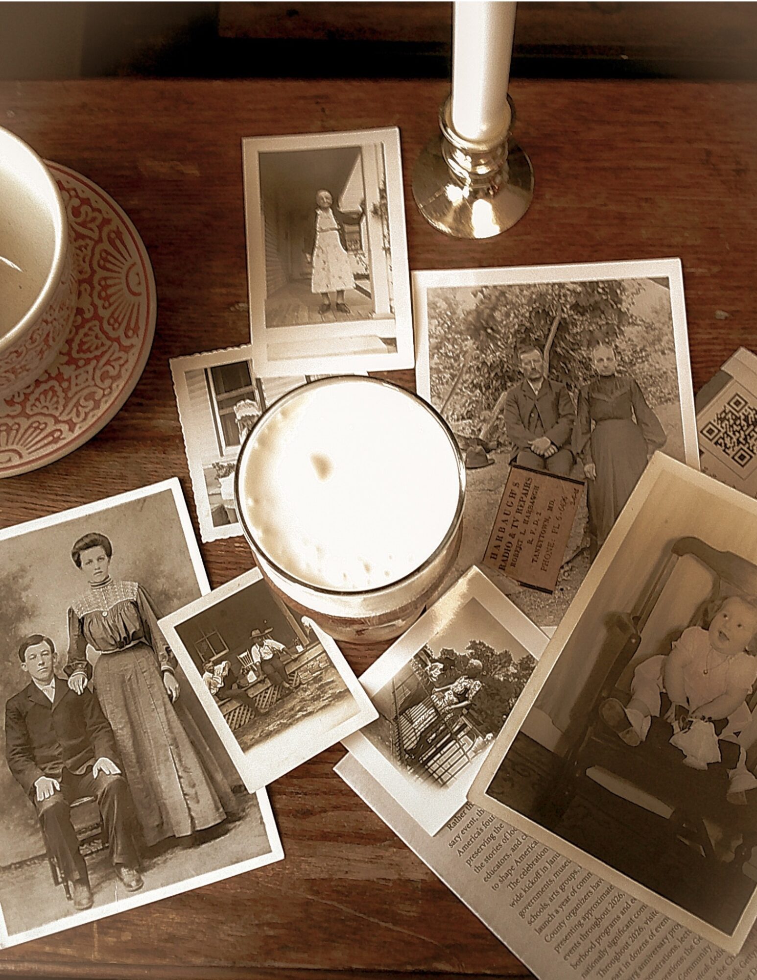 Vintage black-and-white photographs, a lit candle, and a candlestick on a wooden surface, with a decorative bowl nearby.