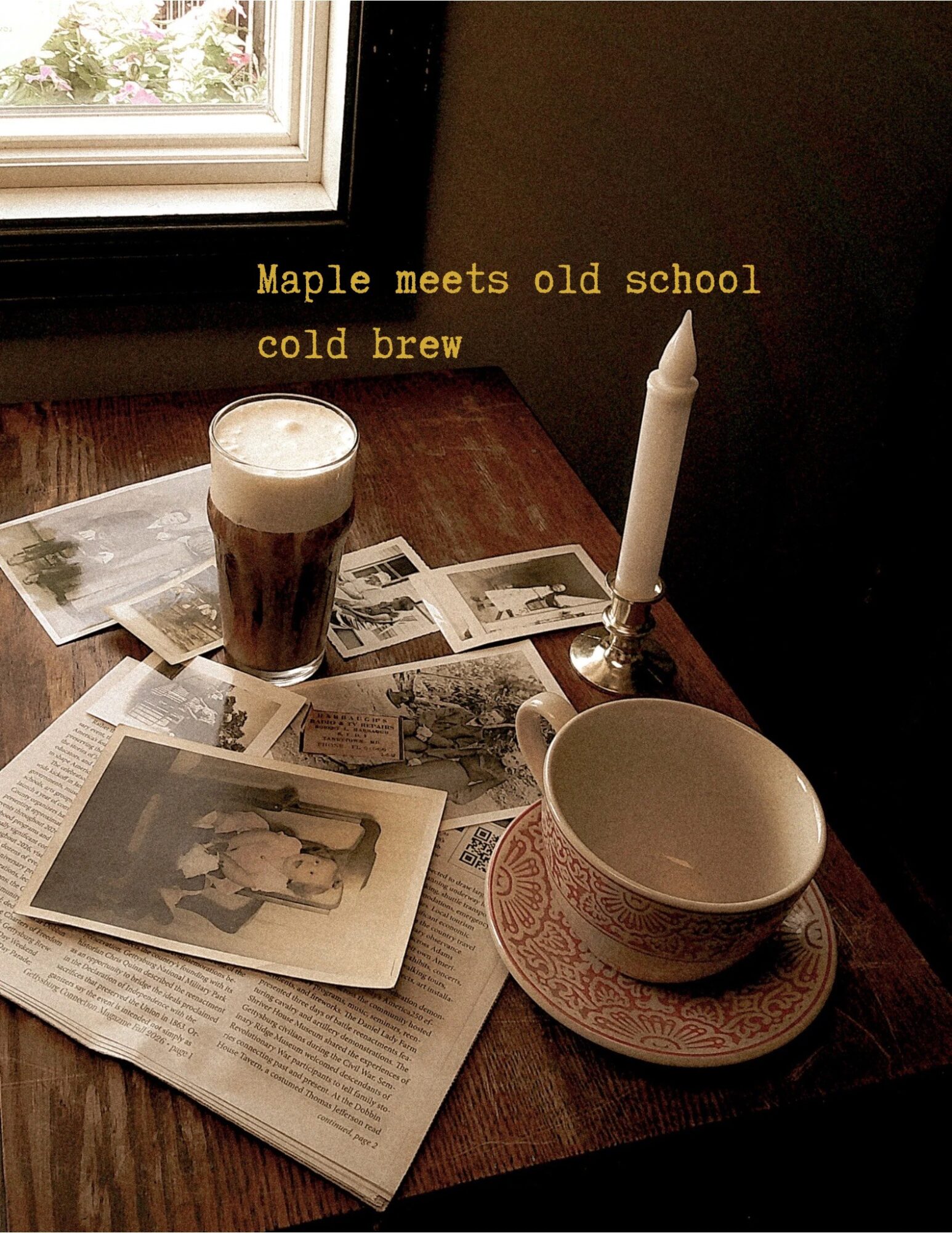 A table with a glass of dark beer, a candle, photographs, a bowl on a plate, and a window in the background.