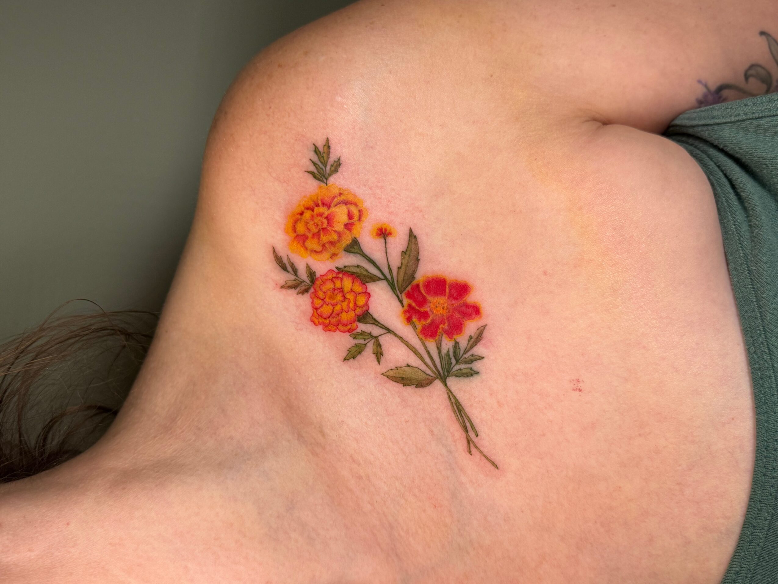Colorful floral tattoo on person's shoulder with orange and red flowers and green leaves.