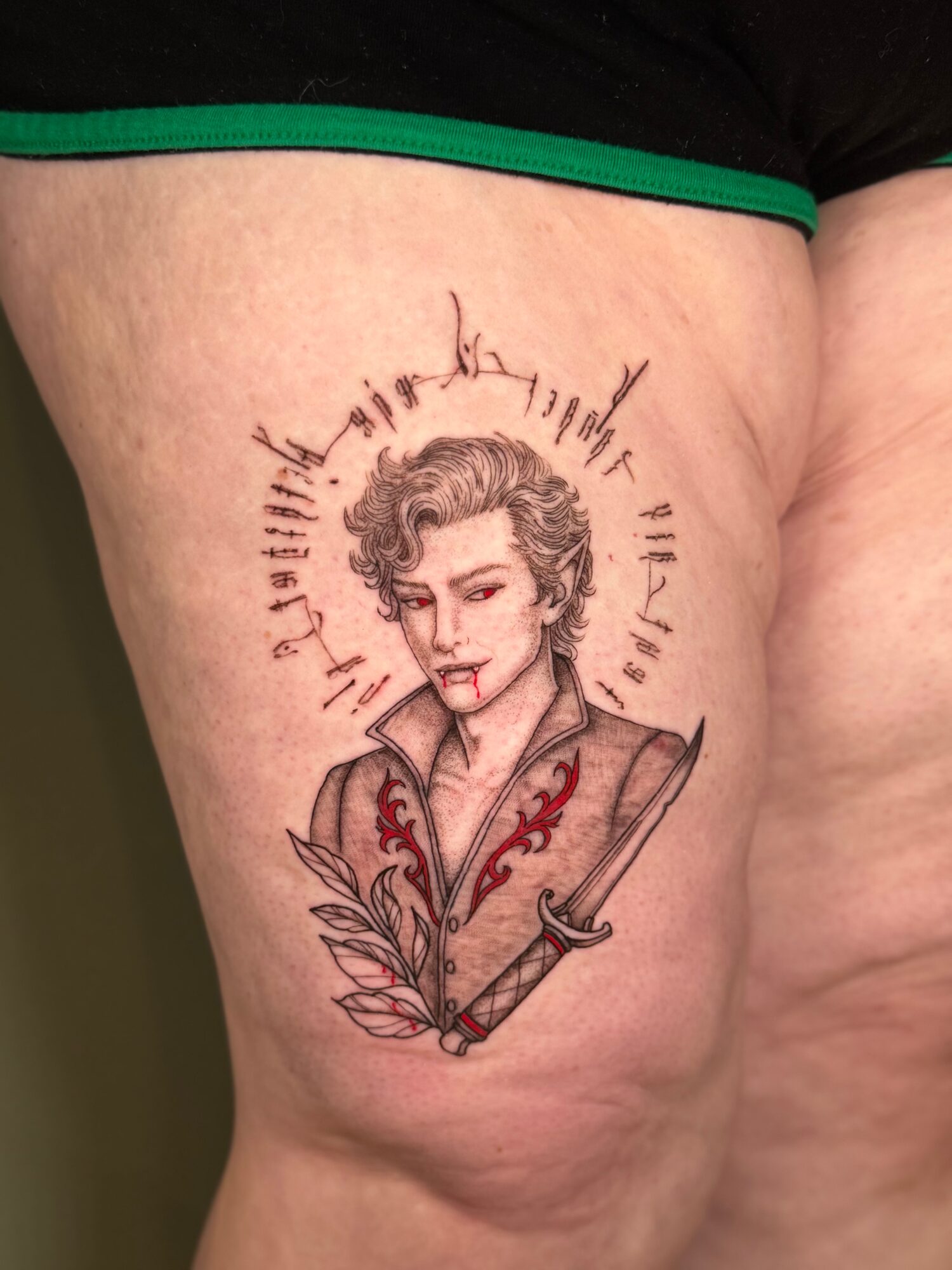 Tattoo of a woman with short curly hair, holding a sword, surrounded by a circular design with text, on thigh.