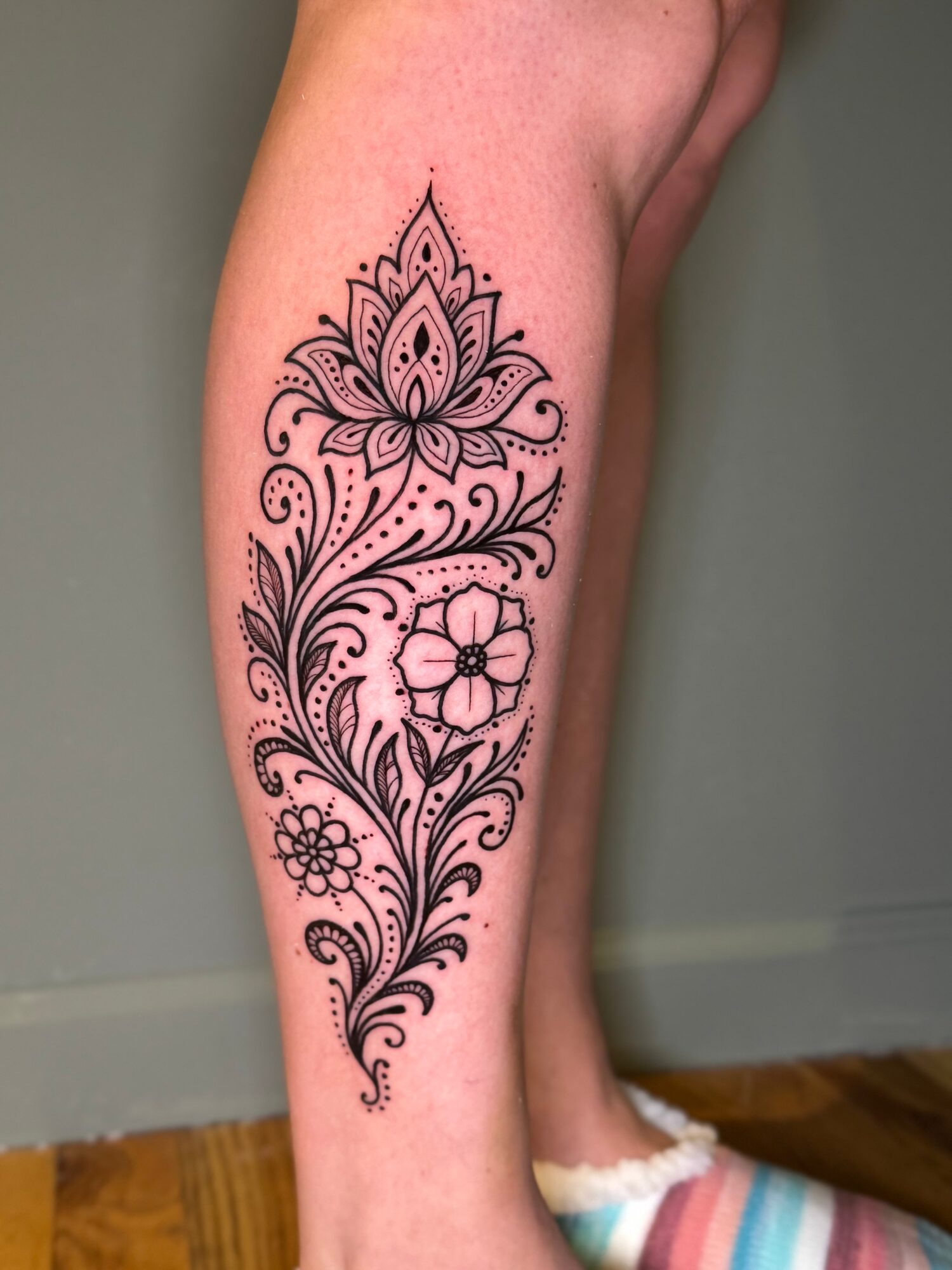 Black floral tattoo with intricate patterns and a pink flower on a person's calf.