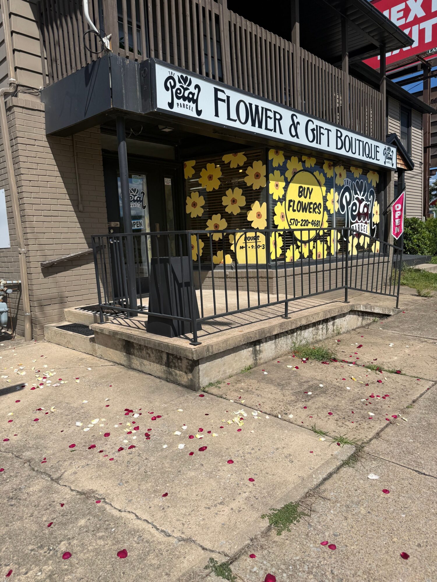 Flower shop entrance with yellow and black floral display, sign reading 'Flower & Gift Shop,' on sidewalk with scattered petals.