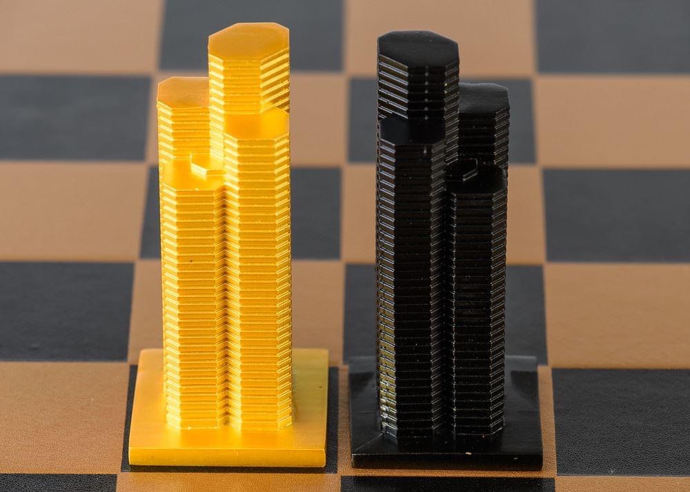 Two stacks of coins, one gold and one black, on a checkered surface, representing a comparison of values.