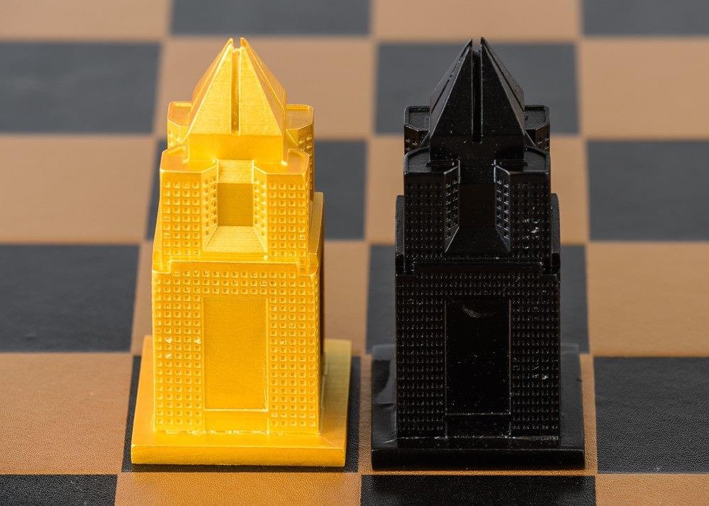 Two small castle-shaped objects, one yellow and one black, placed on a chessboard pattern surface.