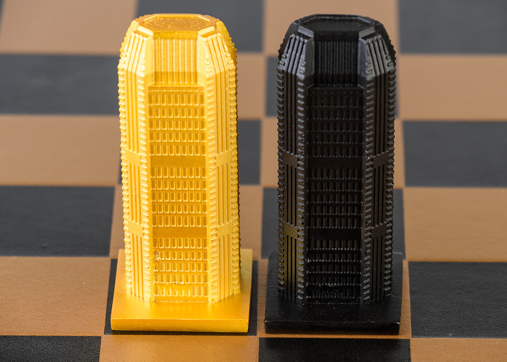 Two LEGO skyscraper models, one yellow and one black, stand side by side on a chessboard-like surface.