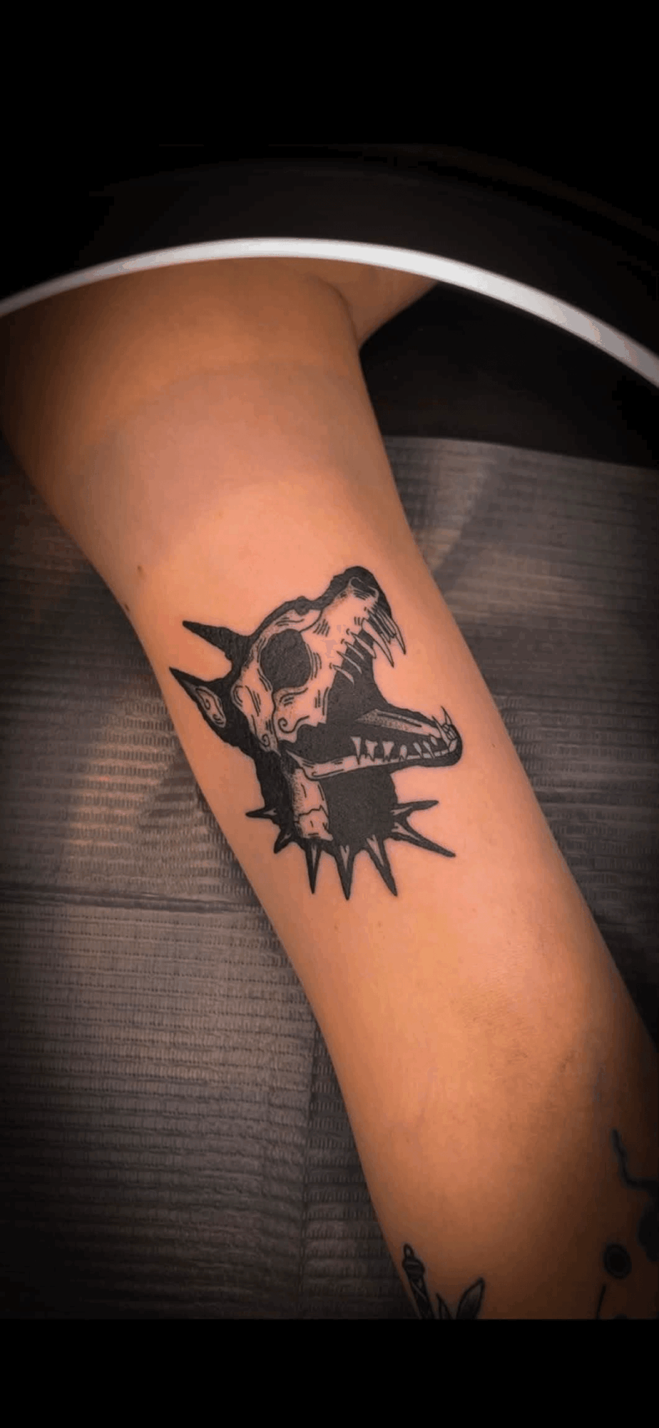 Tattoo of a wolf's head with an open mouth and sharp teeth on a person's arm.