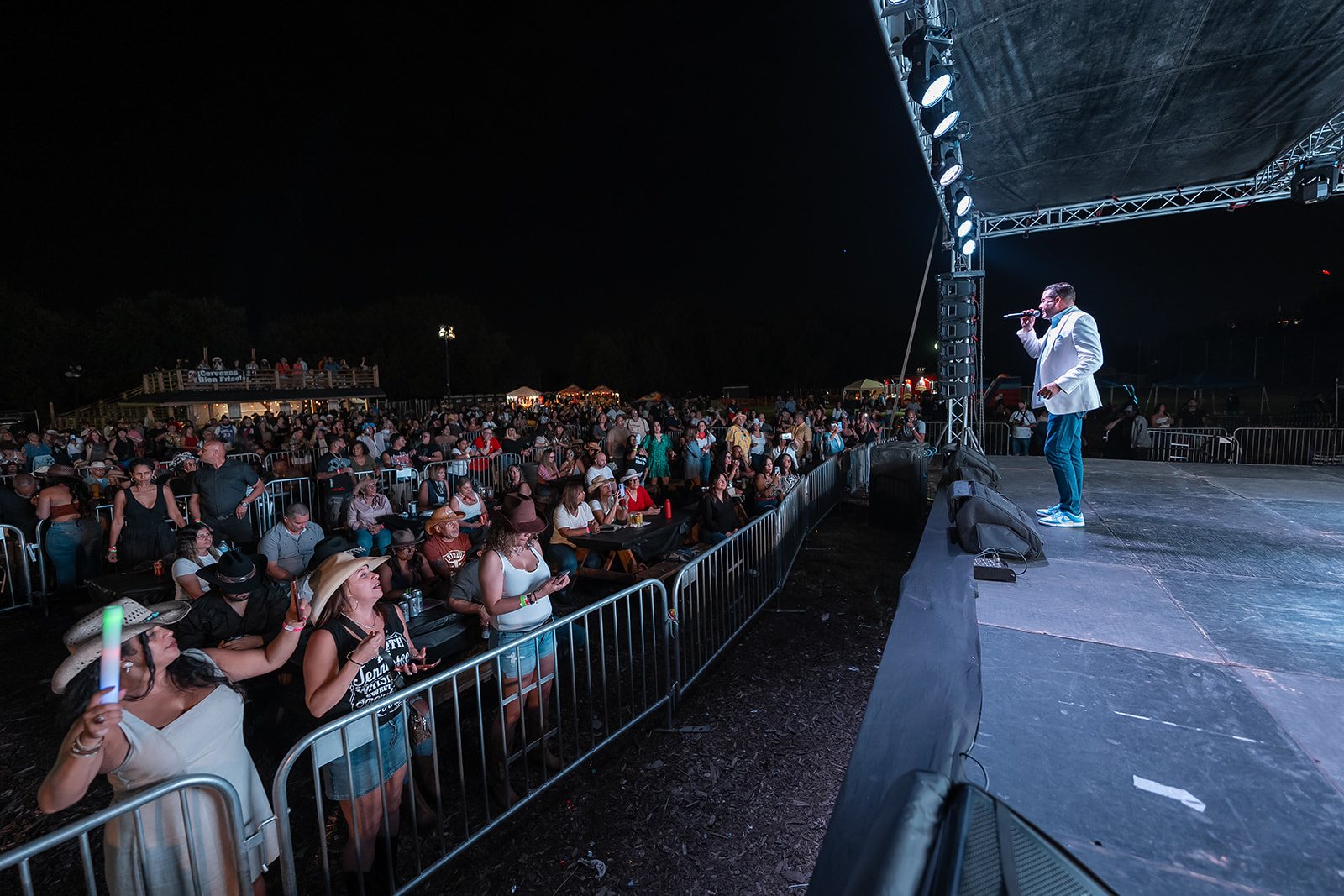 Performer on stage with microphone in front of a large audience at night, stage lighting visible.
