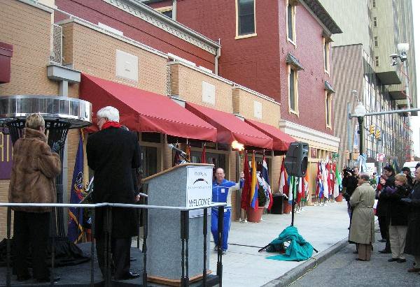 People gather outside a building with red awnings and colorful clothing displays on a city sidewalk.