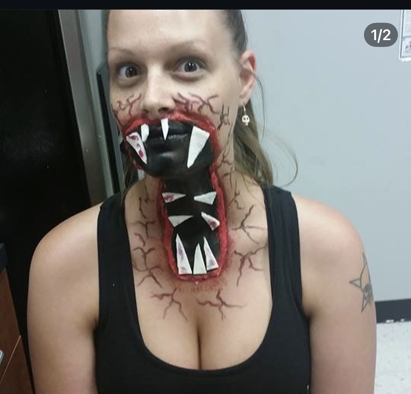 Person wearing a monster mask with sharp teeth and red veins, covering mouth, with a black tank top, in an indoor setting.