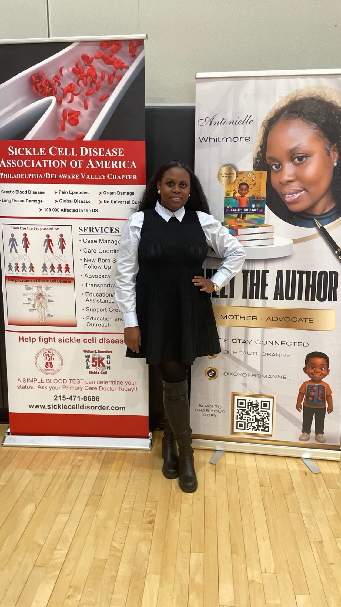 Girl in school uniform standing between two banners, one about sickle cell disease and the other with a woman's photo and text, in a room with wooden floor.