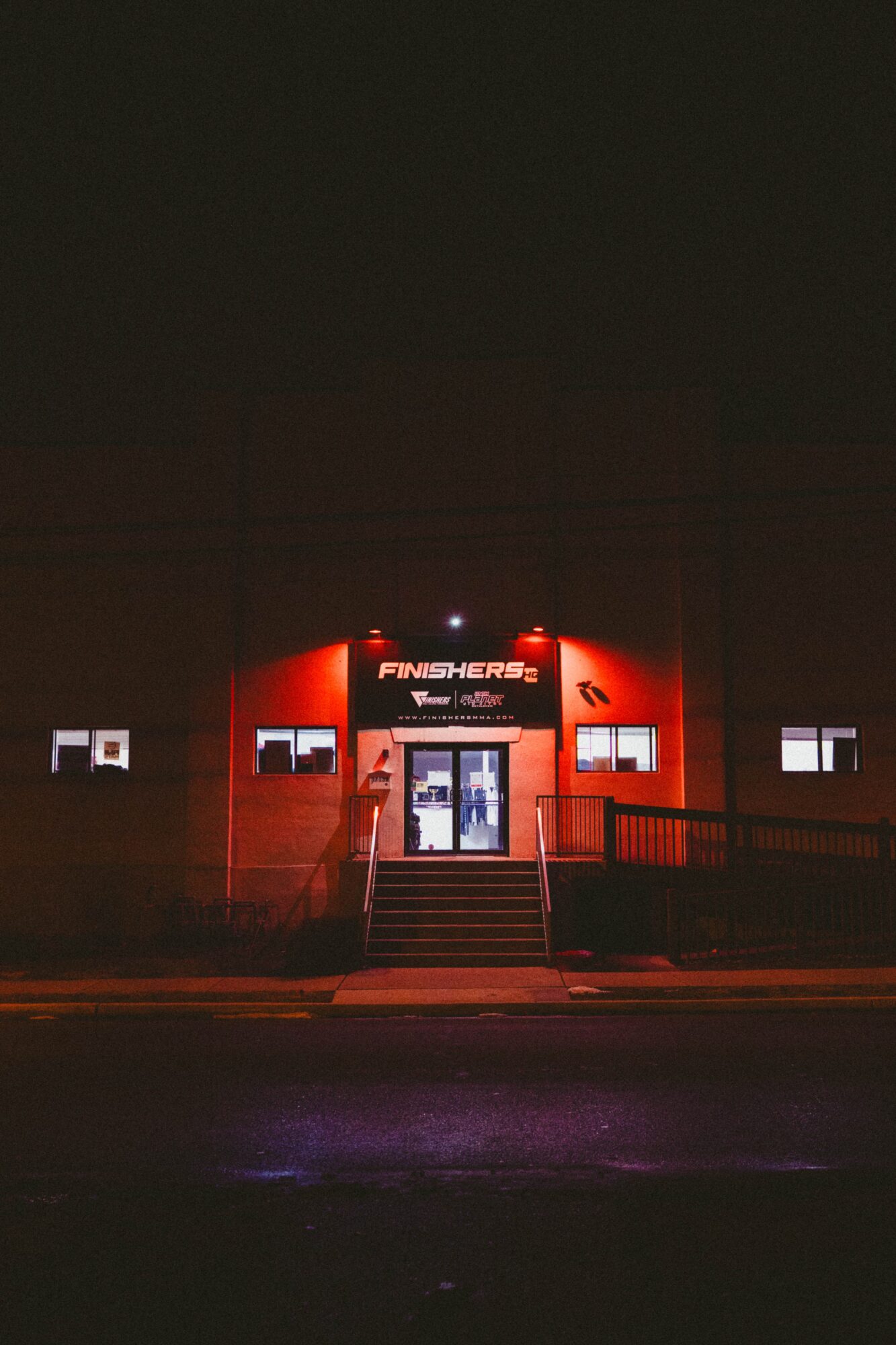 Building entrance illuminated at night with stairs leading up to a door, red and white signage, dark sky.