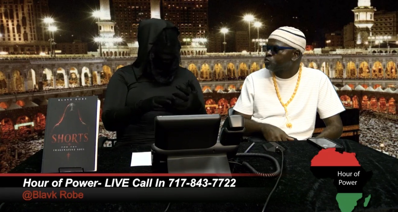 Two people sit at a table with a laptop, one in black clothing and the other in white, outdoors at night.
